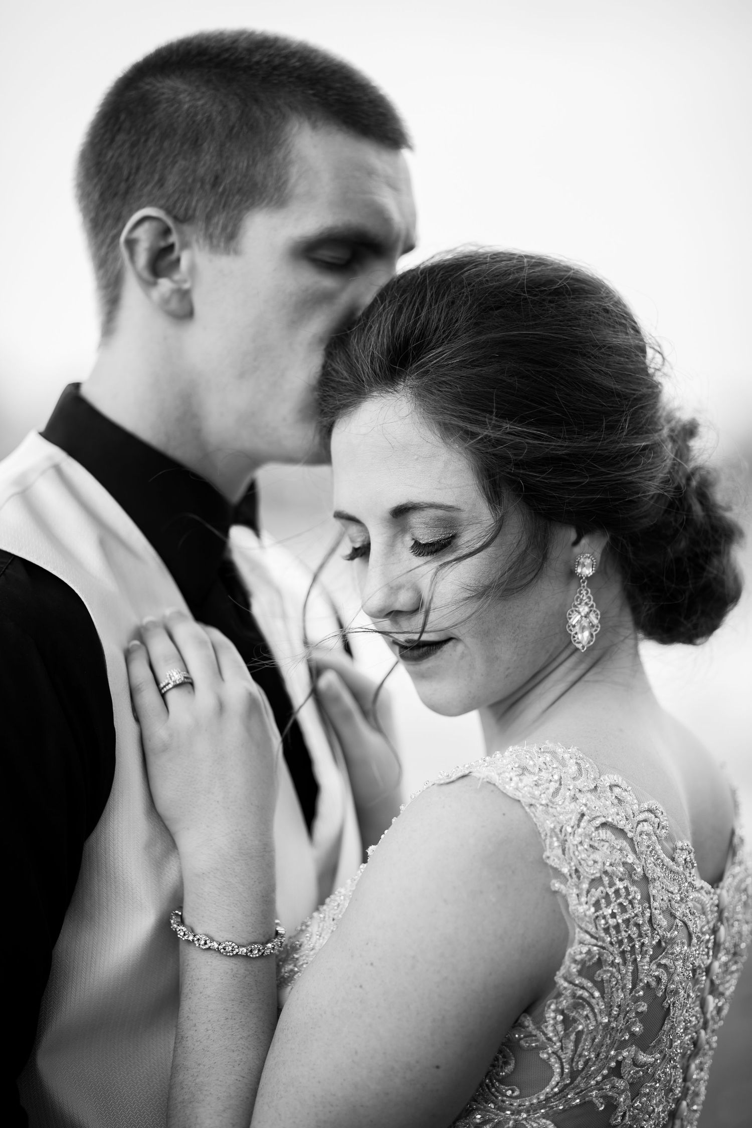Intimate black and white wedding portrait showing tender moment between newlyweds with delicate lace dress details.