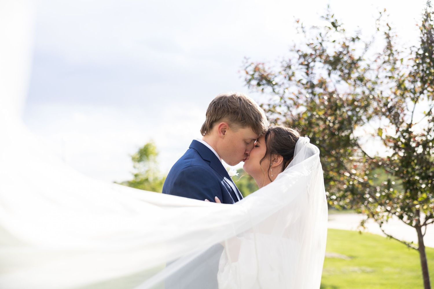 Bride and groom sharing a romantic moment under a flowing white veil outdoors on their wedding day.