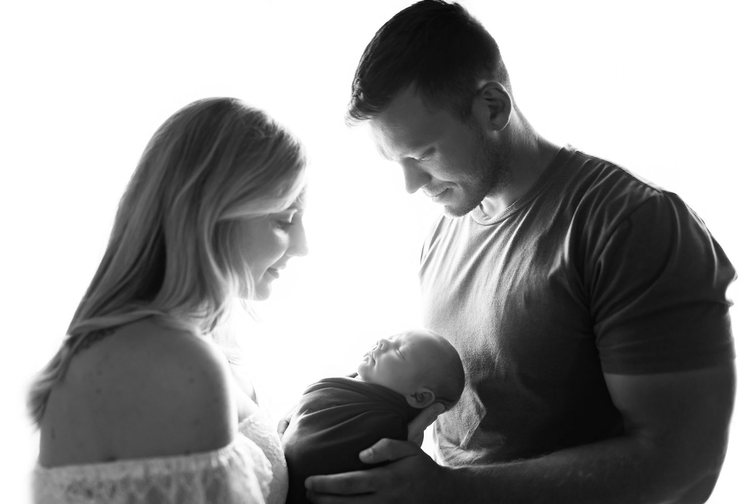 A backlit black and white portrait of new parents with their baby.