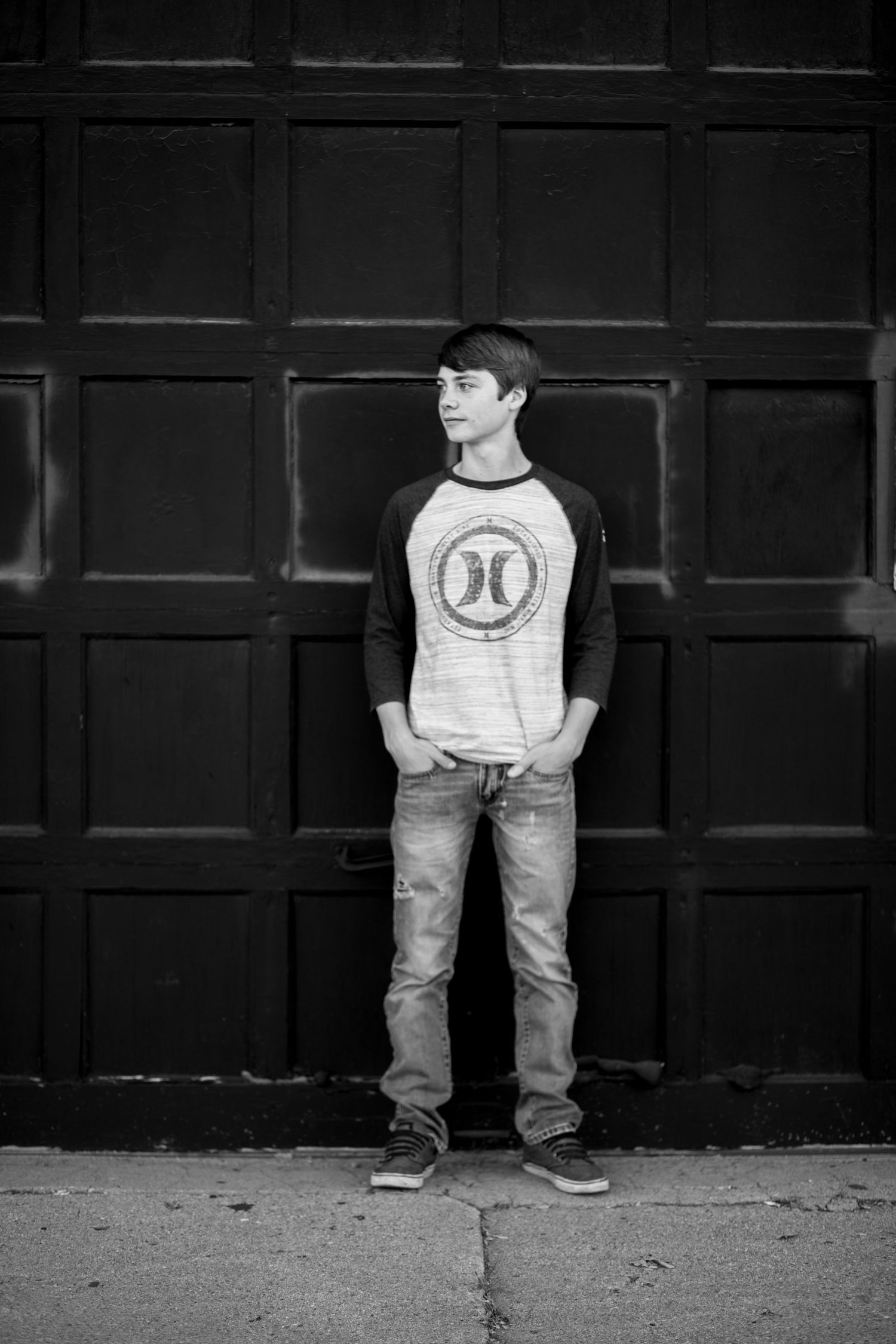 Person poses against dark paneled wall wearing baseball style shirt.