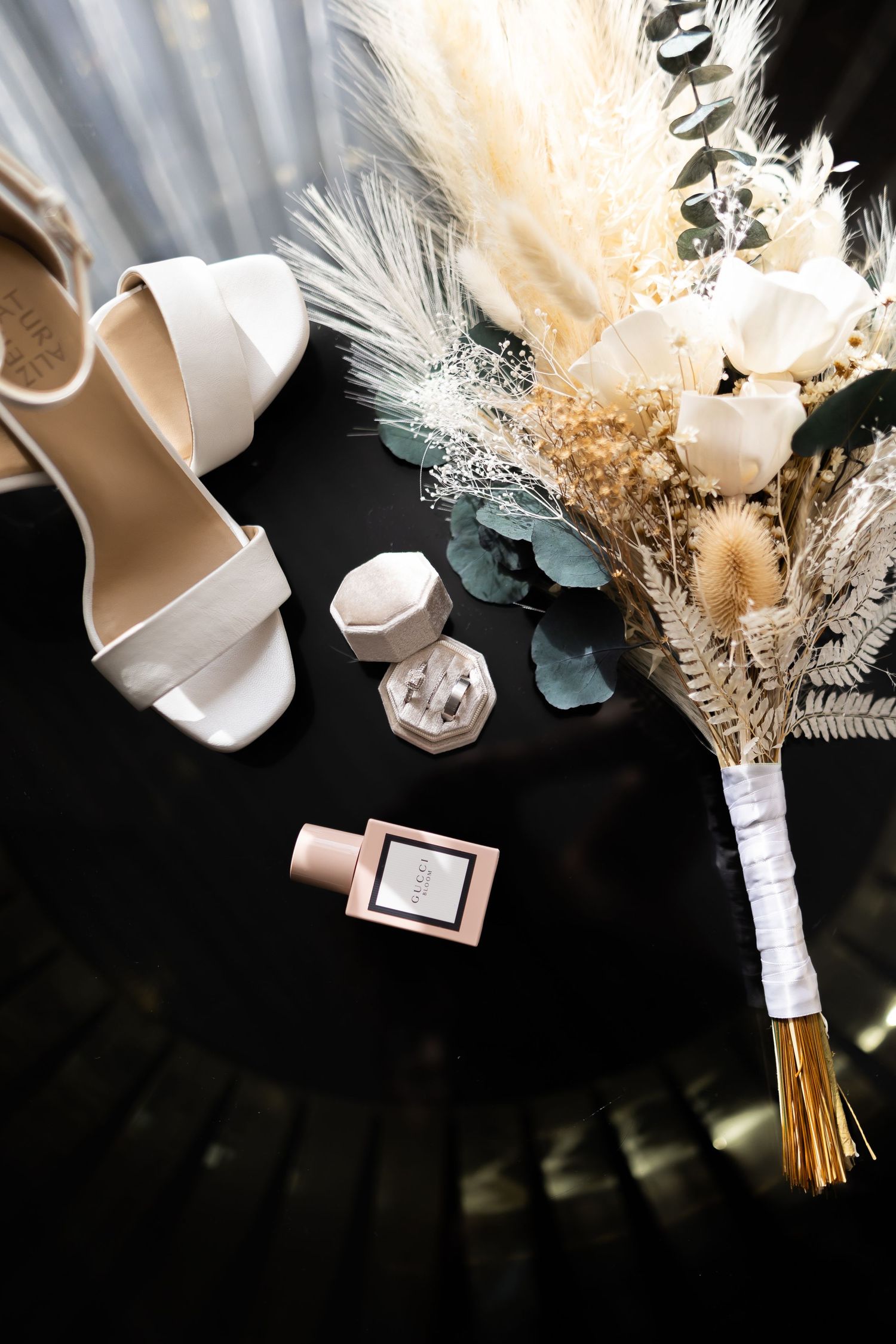 Wedding accessories flatlay with white shoes, perfume bottle and dried flower bouquet.
