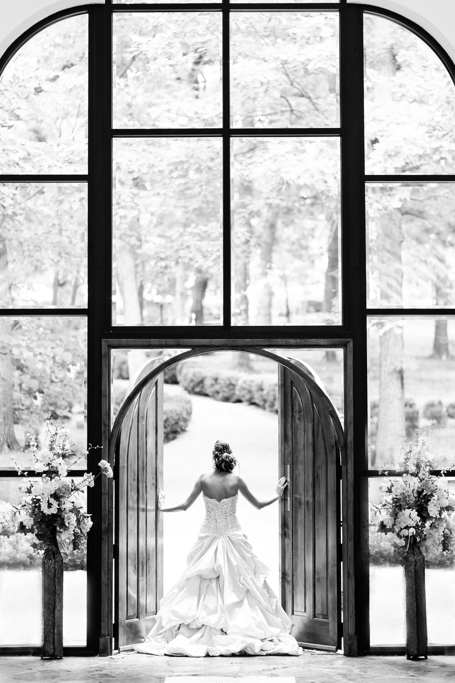 A dramatic black and white photo of a bridal silhouette framed in an arched chapel doorway.