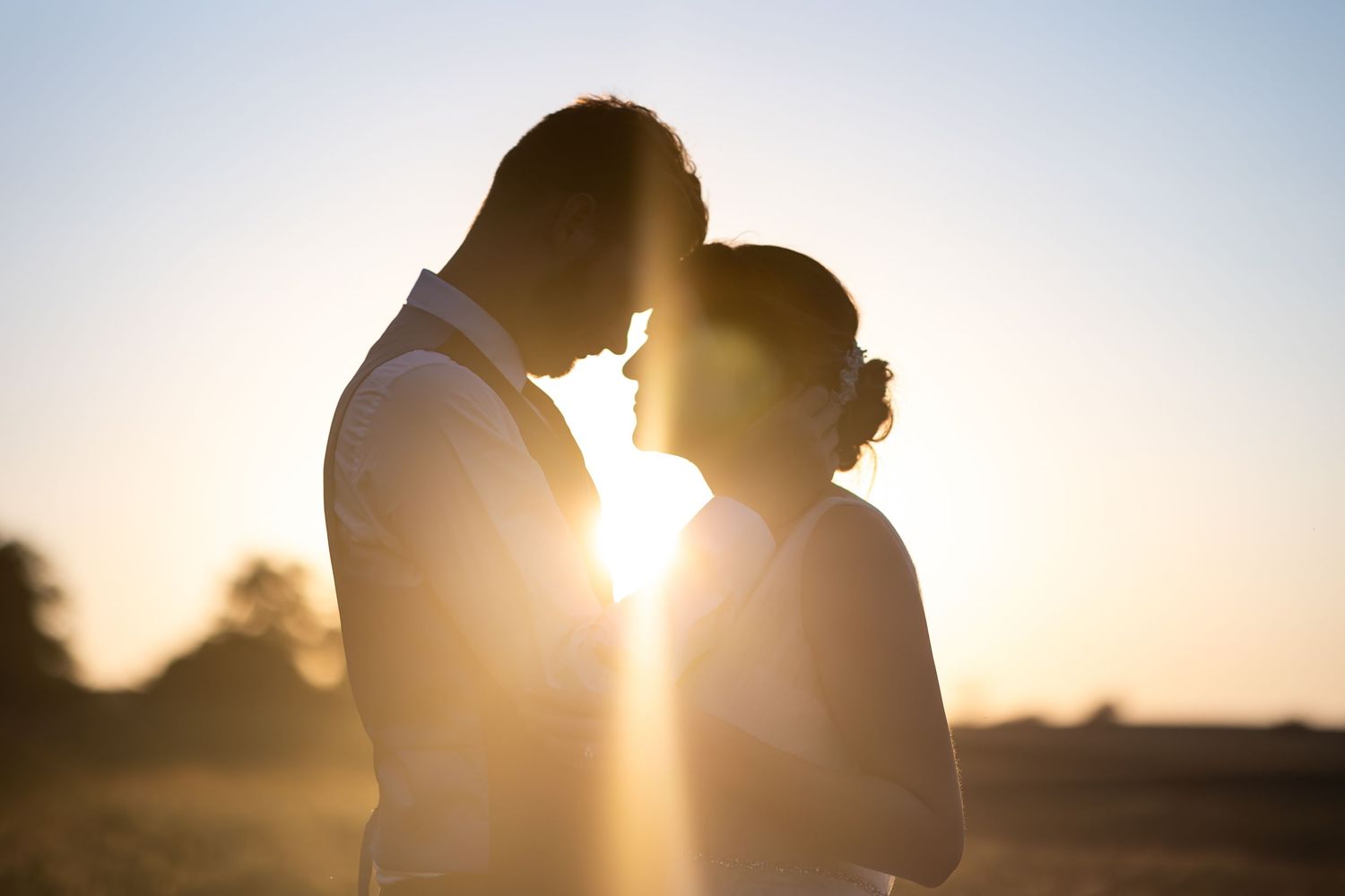 Silhouetted couple stands close together in warm sunset light creating romantic backlit glow.