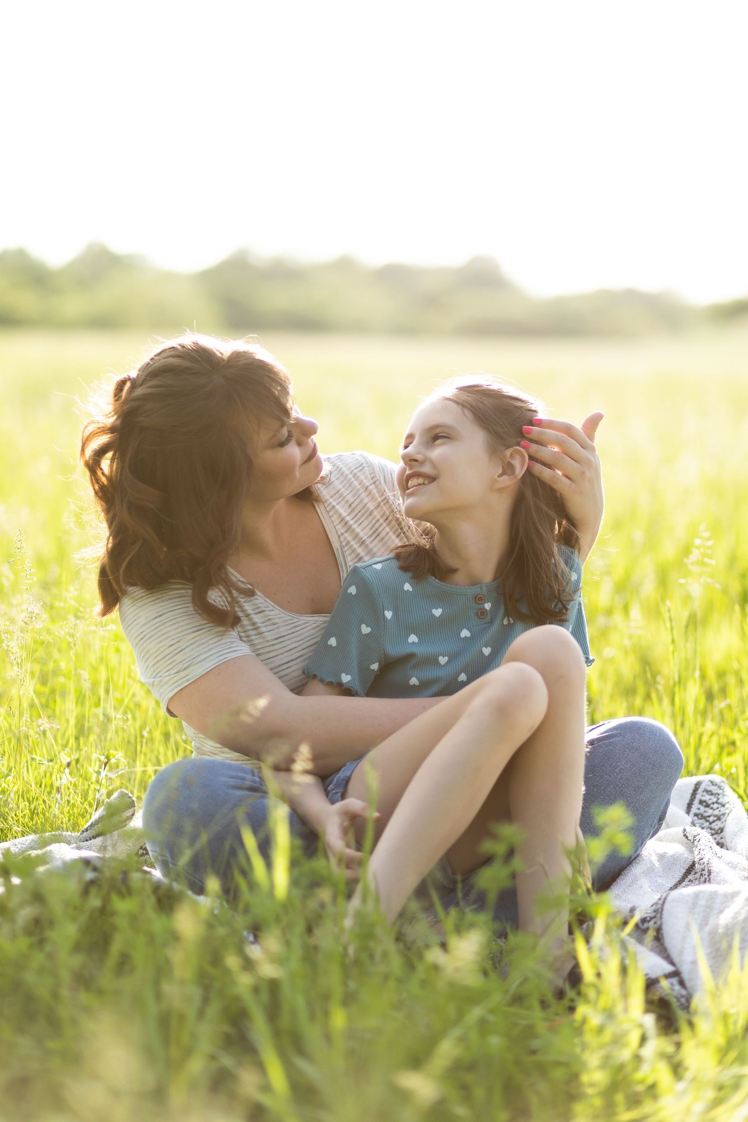 Two people share a tender moment together while sitting in a sunny meadow.
