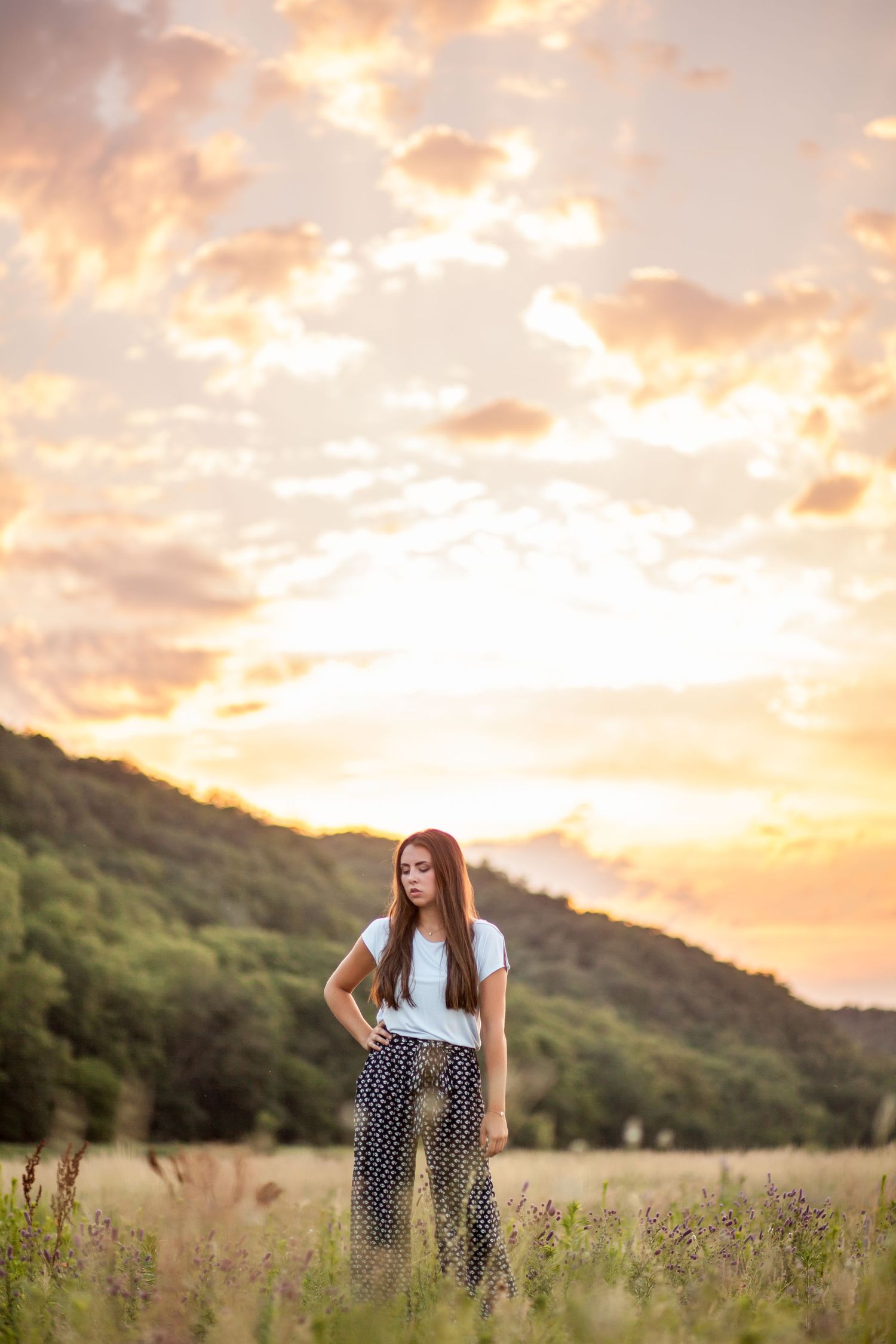 Person stands in field during golden sunset with mountains in background.