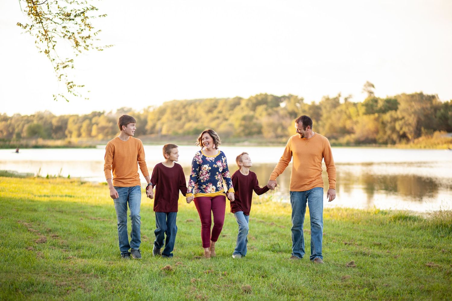 Group walks together on grassy hill beside lake during golden sunset hour in autumn landscape.