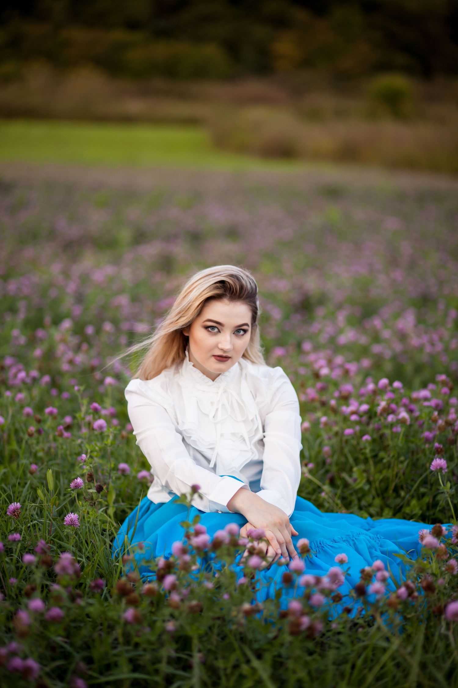 Portrait in a field of purple wildflowers with white blouse and blue skirt.