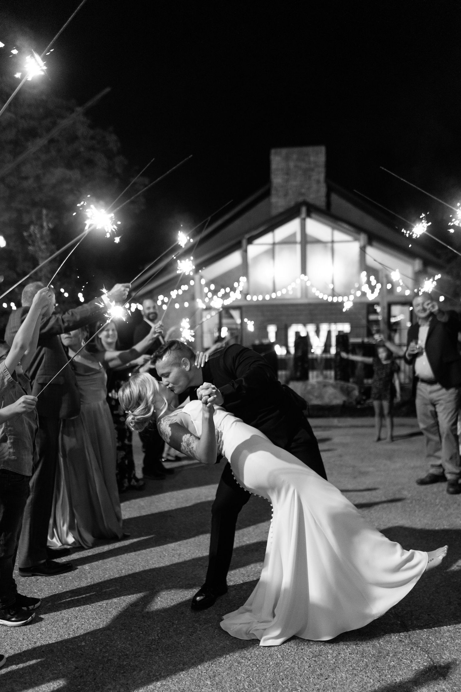 Romantic wedding couple shares a dramatic dip kiss under sparklers at their outdoor nighttime reception.