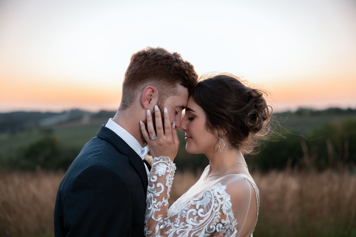 Romantic bride and groom sharing an intimate moment at sunset in a golden field, wearing elegant wedding attire.