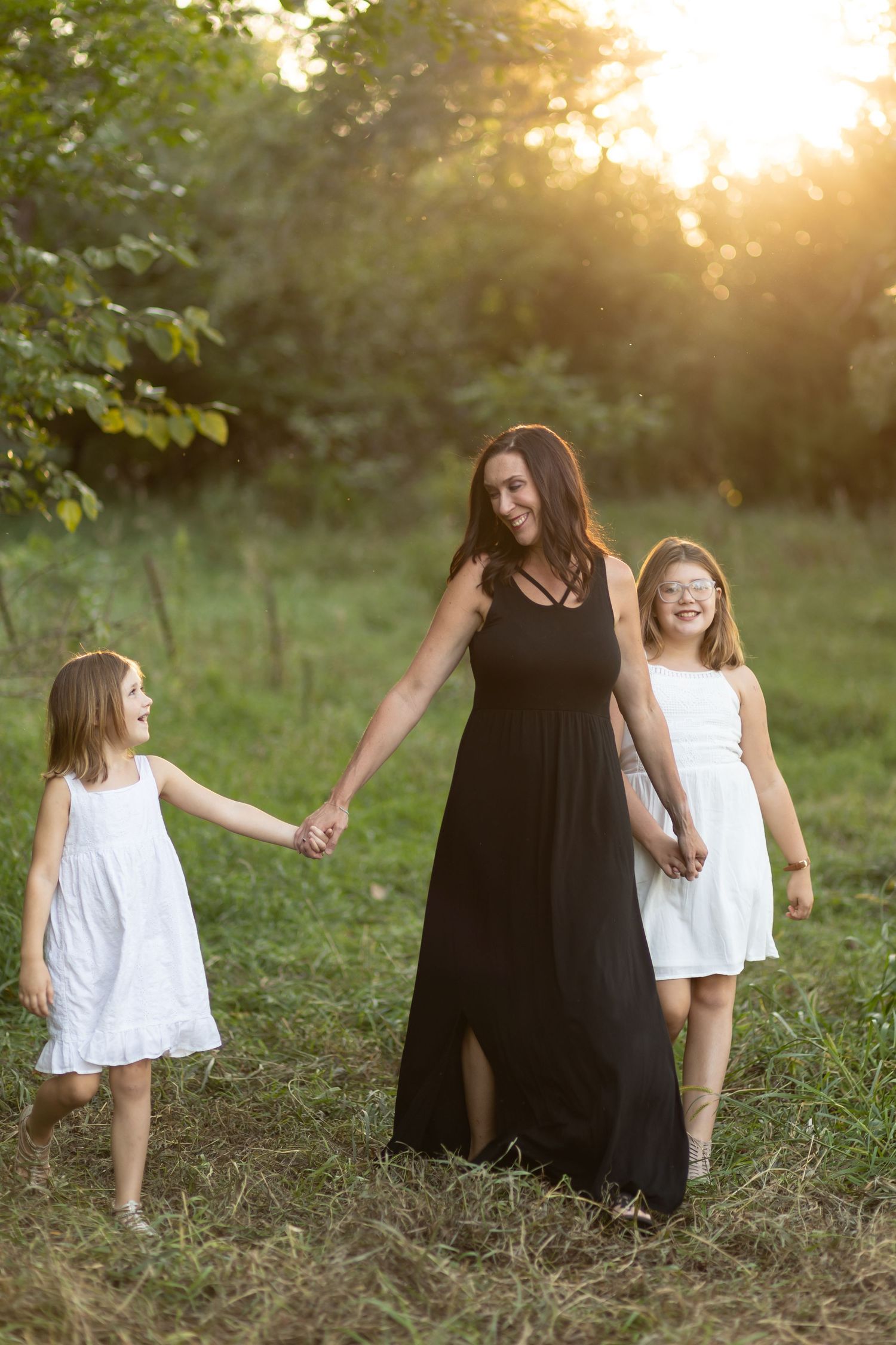 Three figures walk together holding hands through a sunlit meadow at golden hour.