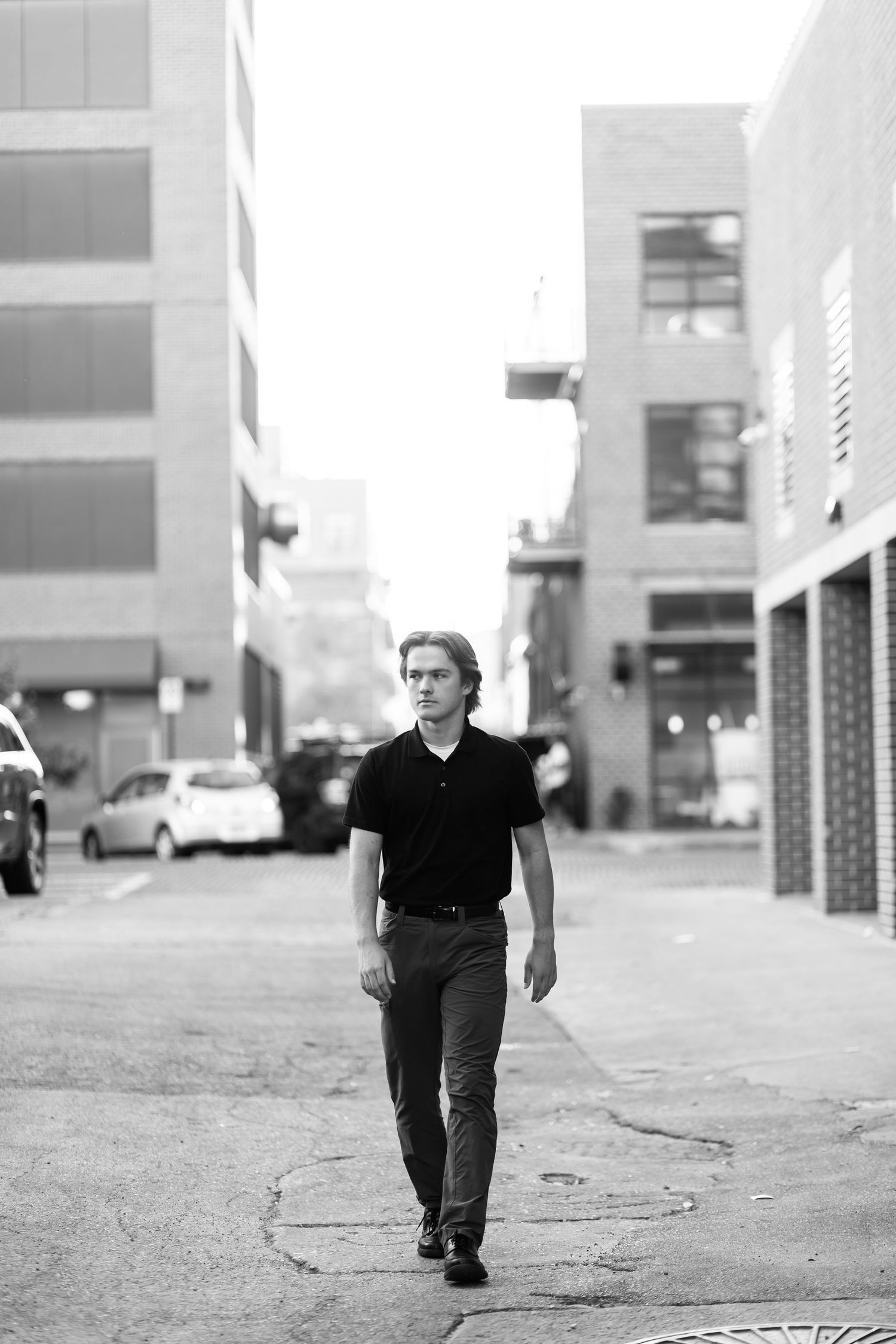 Person in black outfit walking alone on urban sidewalk in black and white photo.