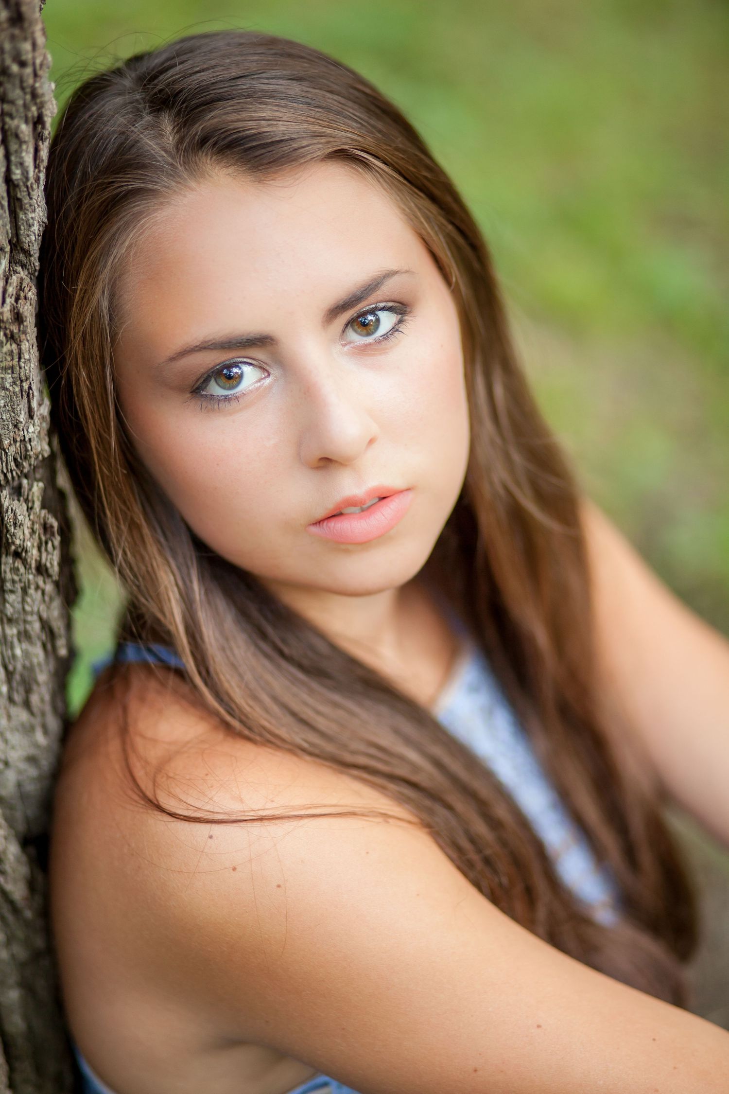 Portrait of person with long brown hair leaning against tree in natural setting.