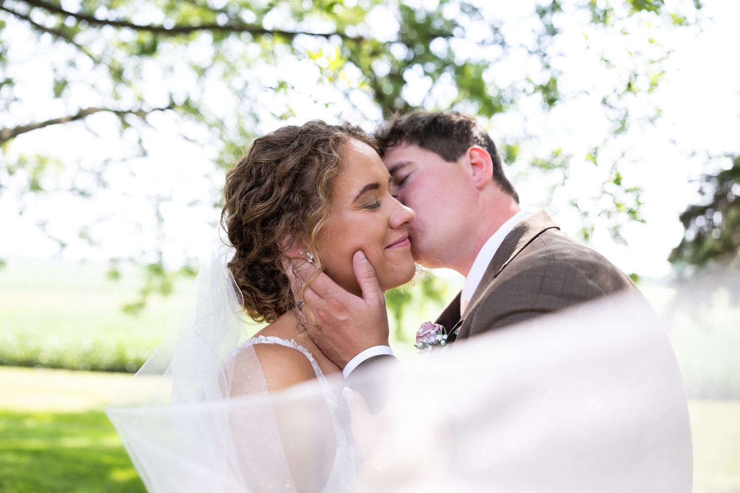 Spring wedding portrait captured through blossoming tree branches in soft lighting.
