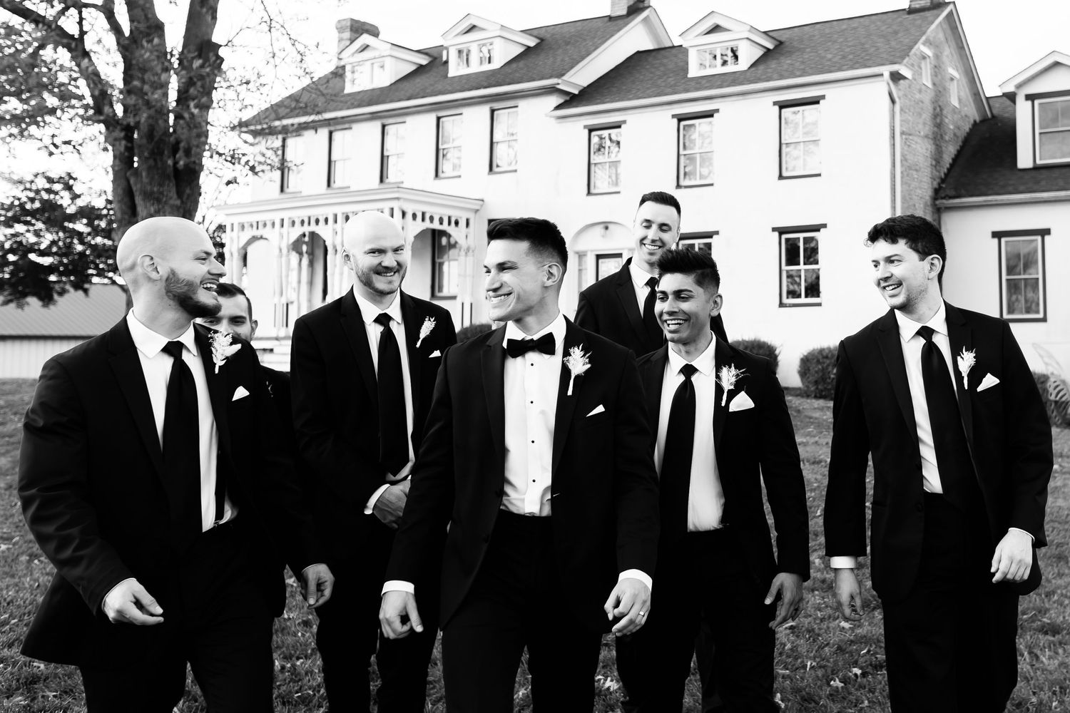 Groomsmen sharing a candid moment outside a classic mansion in black and white.