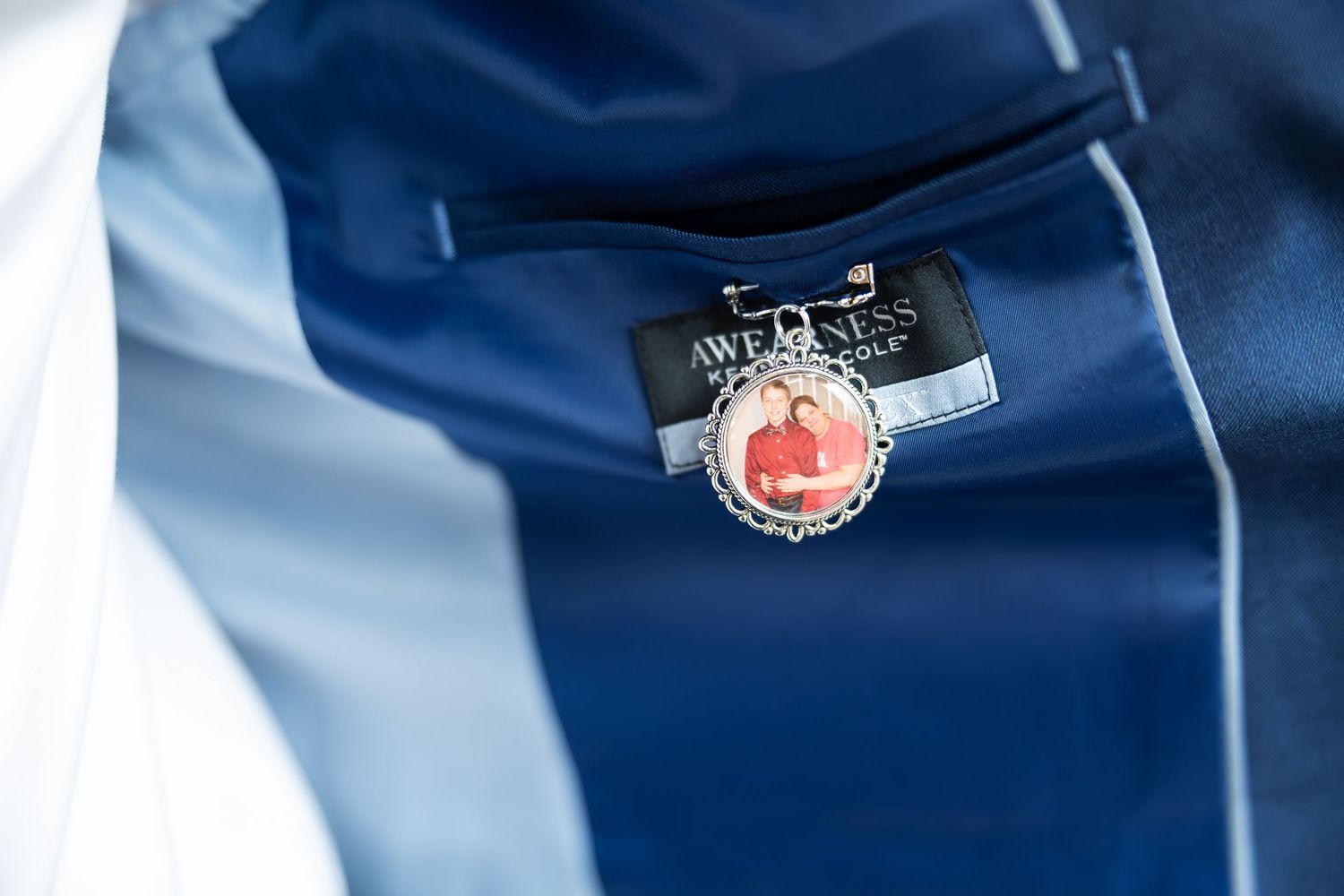 Close-up of a wedding boutonniere charm with a couple photo pinned to a navy blue suit lapel.