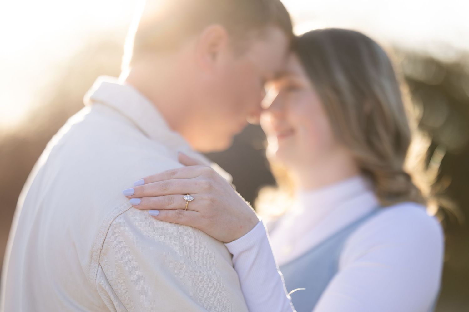Intimate engagement photo of couple embracing in warm sunset light.