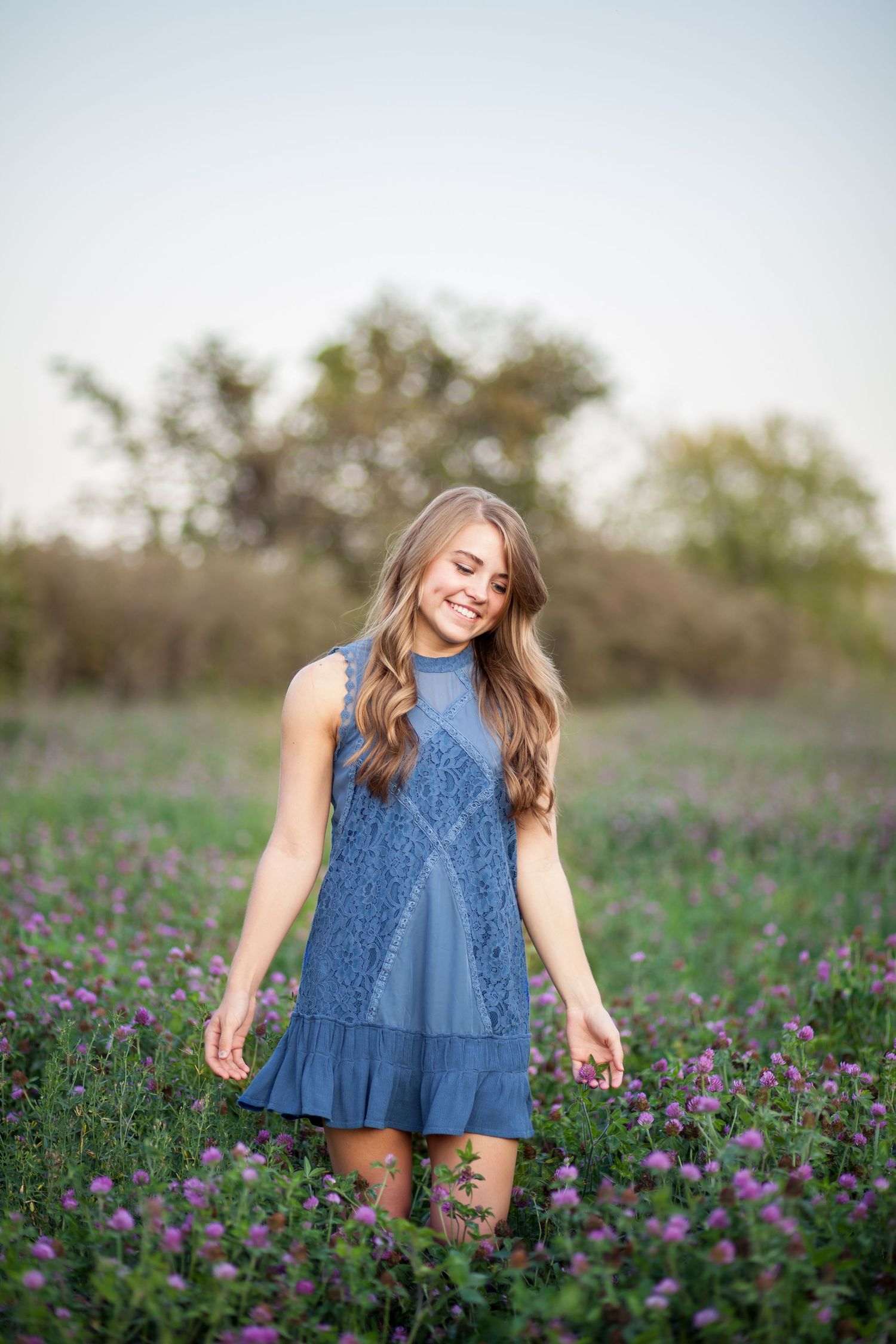 Woman in blue dress twirls joyfully through a field of purple wildflowers at sunset.