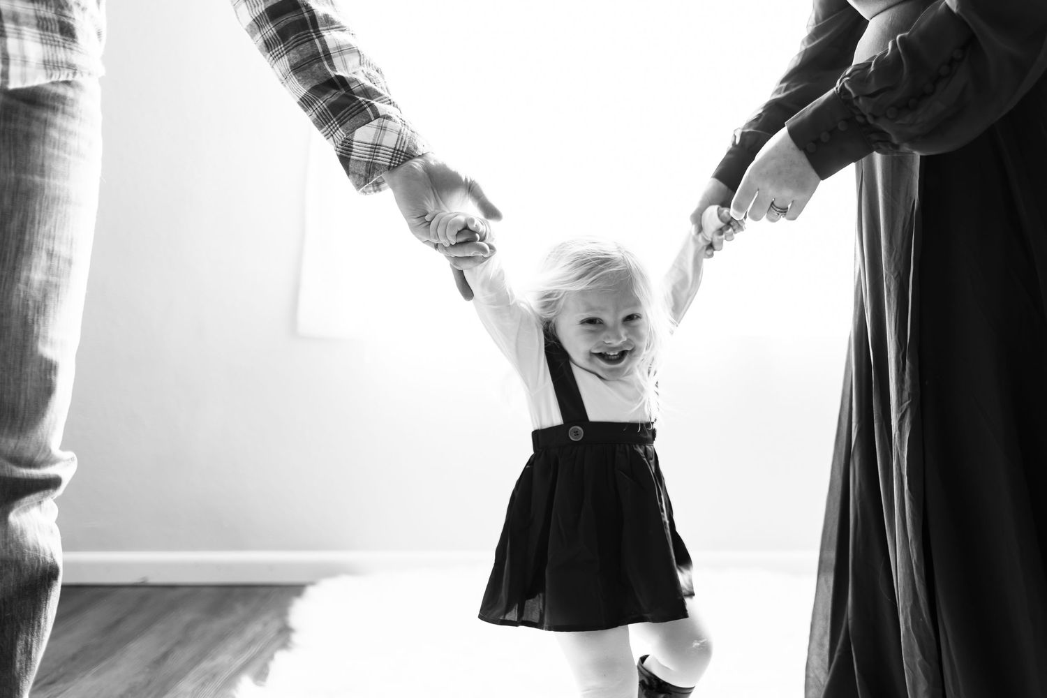 Black and white photo of a toddler learning to walk while holding hands with adults.