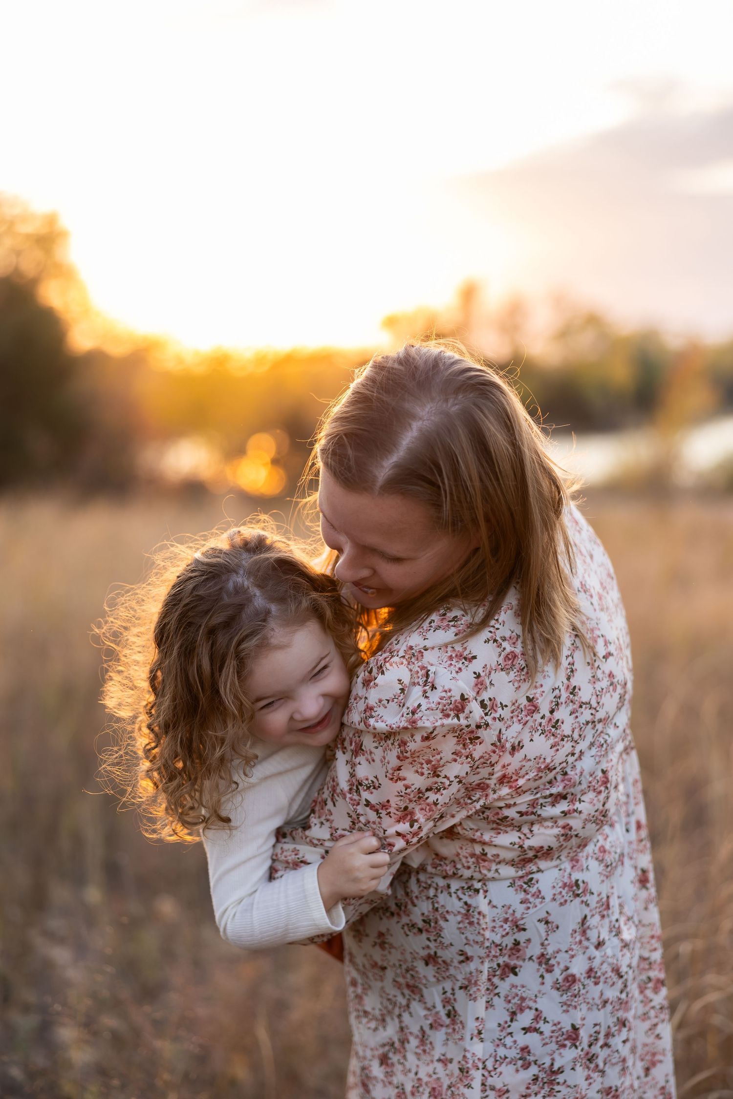 Mother and child sharing joyful embrace in golden sunset lit field.