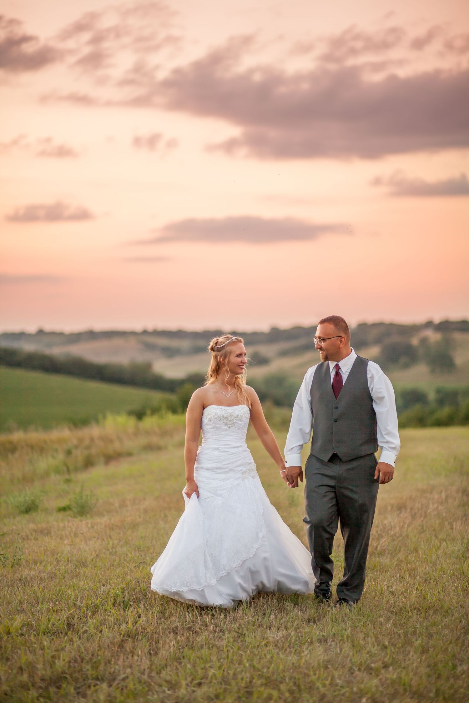 Sunset wedding portrait of couple walking hand in hand across rolling countryside hills.
