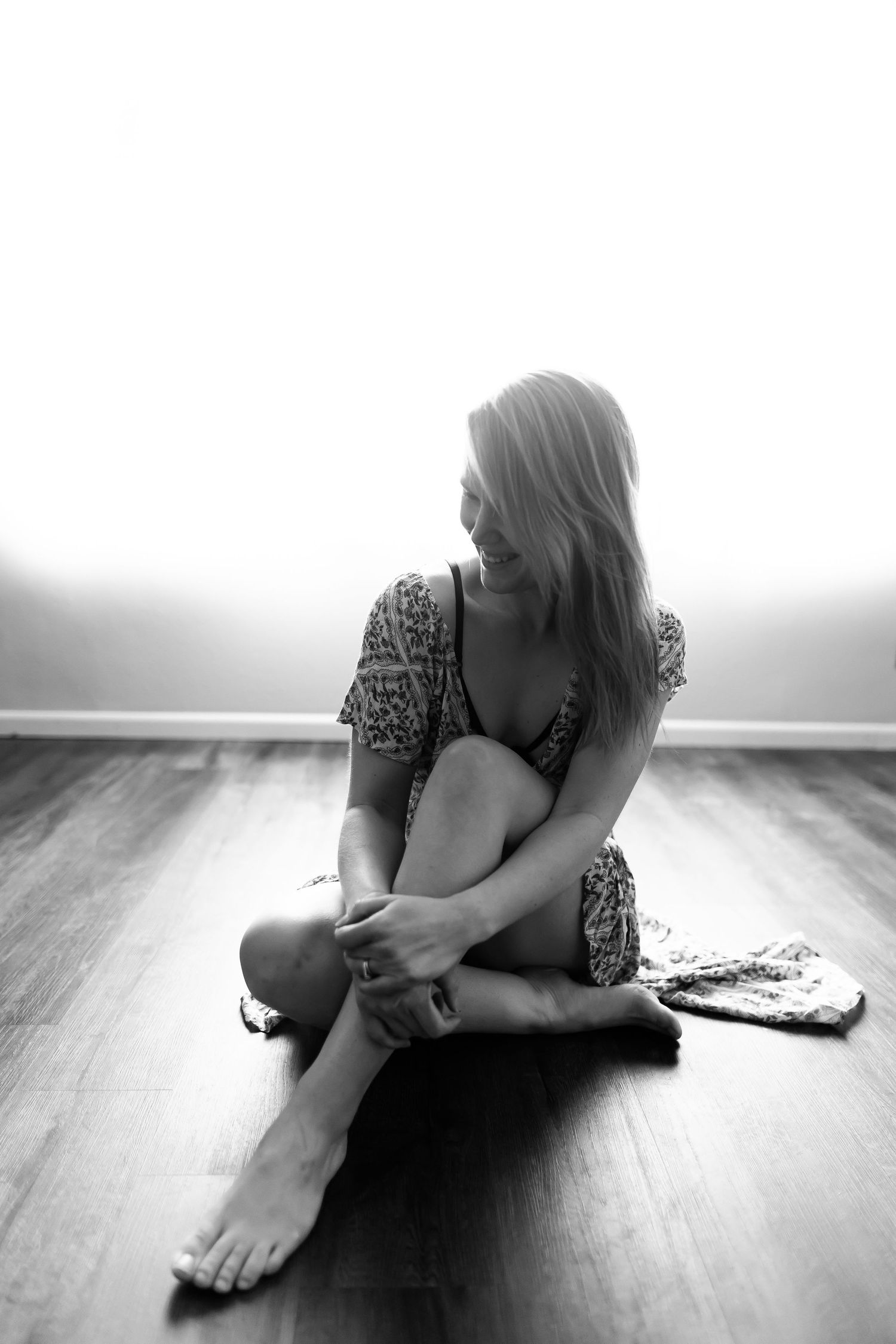 Artistic black and white portrait of woman sitting on hardwood floor.