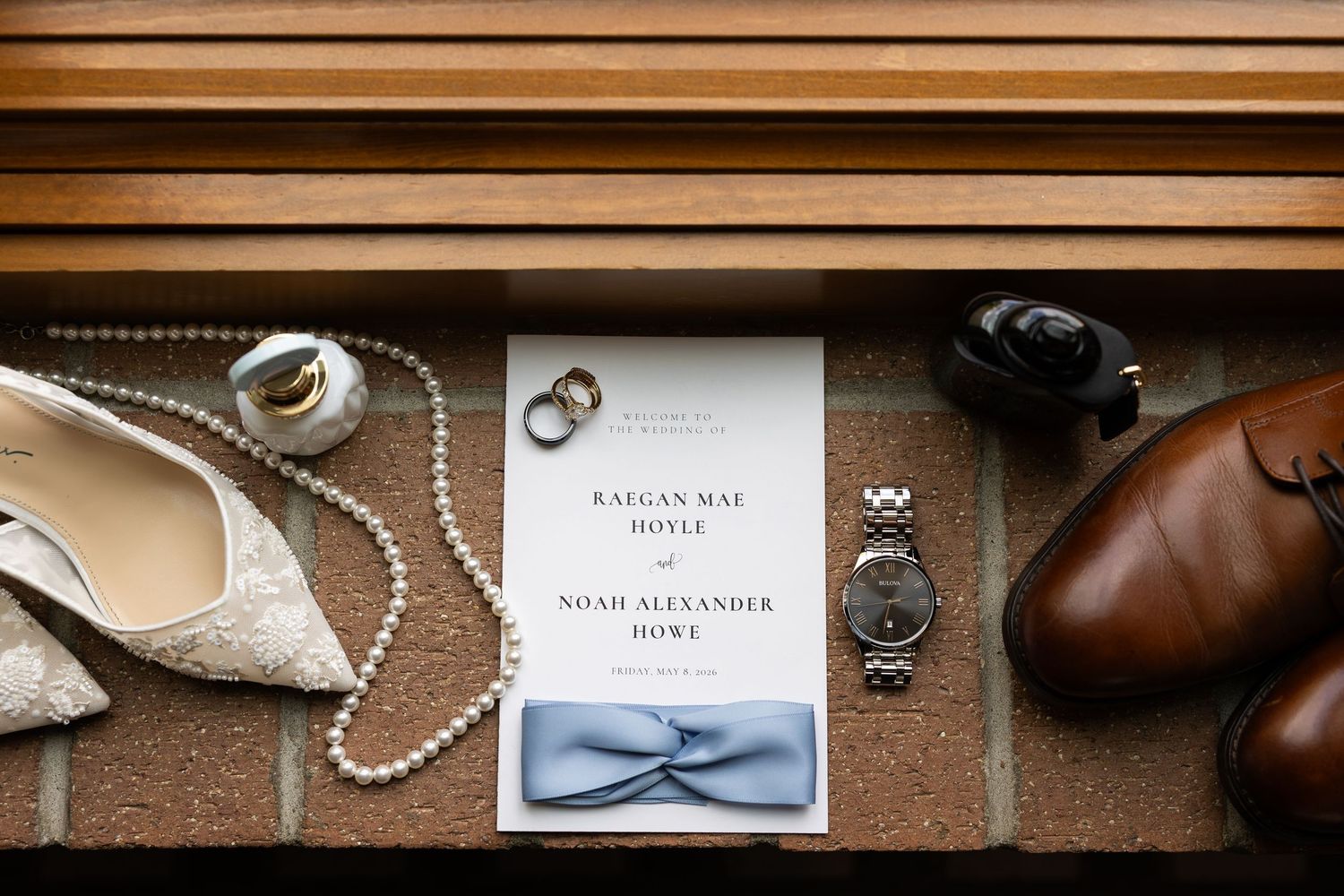 Wedding flat lay featuring invitation for Raigan Mae Hoyle and Noah Alexander Howe, rings, bow tie, watch, heels, pearls, and dress shoes.