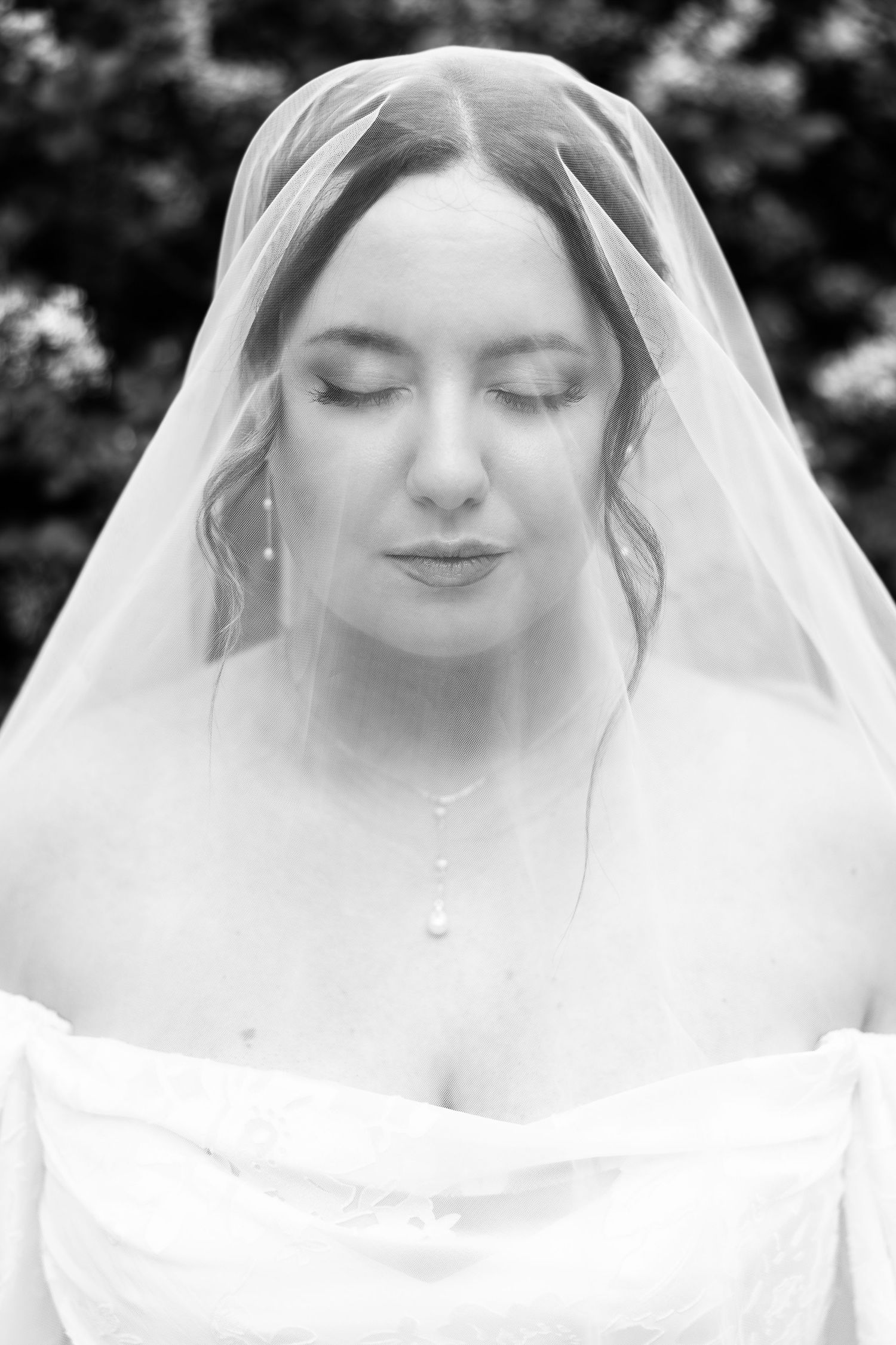 Black and white portrait of a bride with closed eyes wearing a veil and pearl necklace on her wedding day.