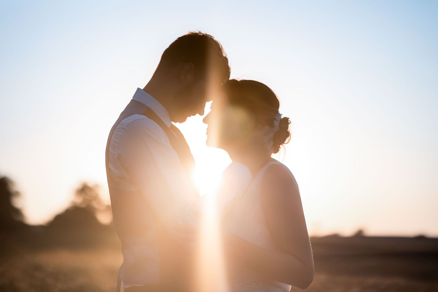 Romantic silhouette of a couple sharing an intimate moment at sunset in an open field on their wedding day.