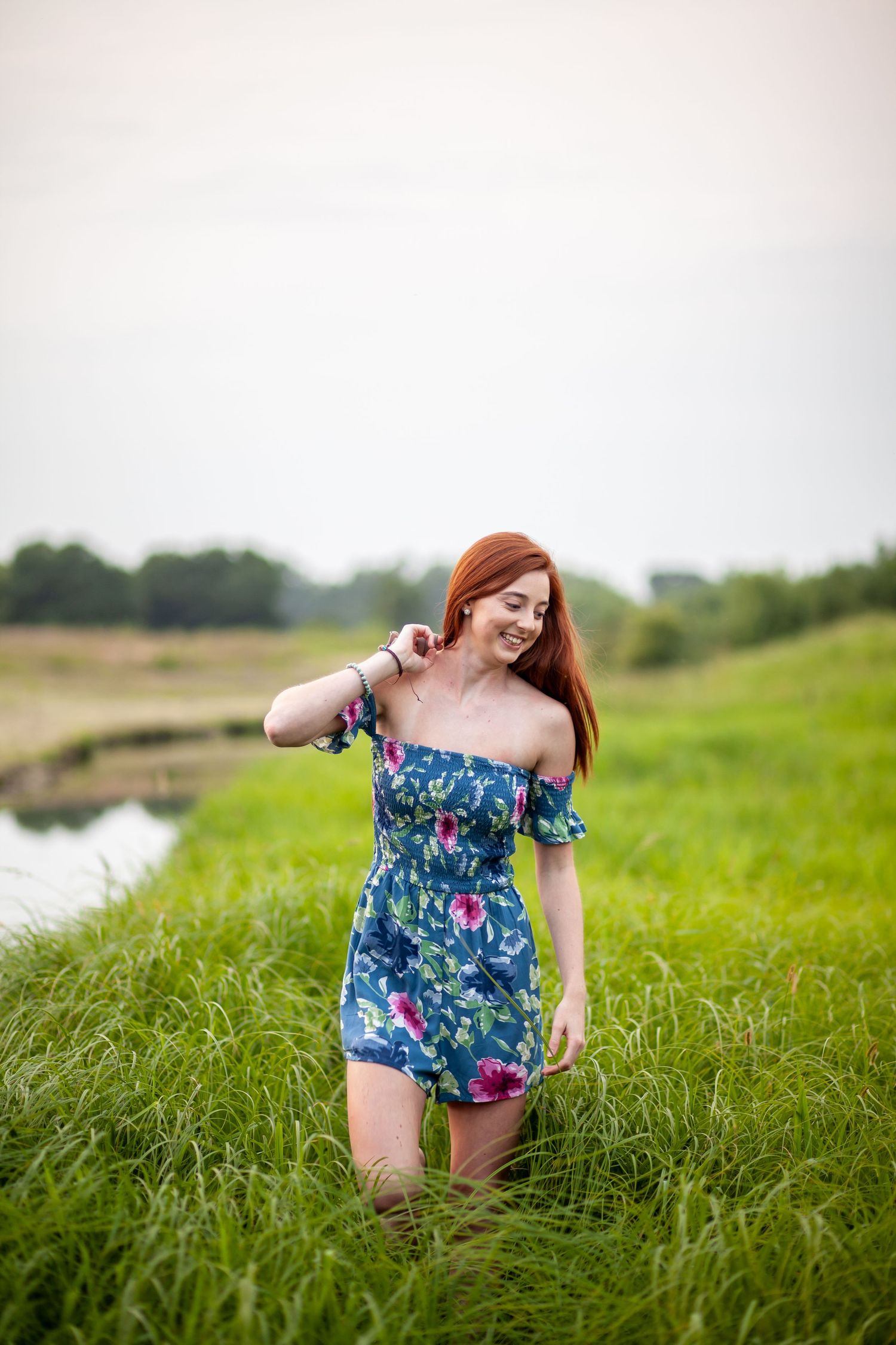 A floral blue summer dress flows in a grassy field near a stream on a sunny day.