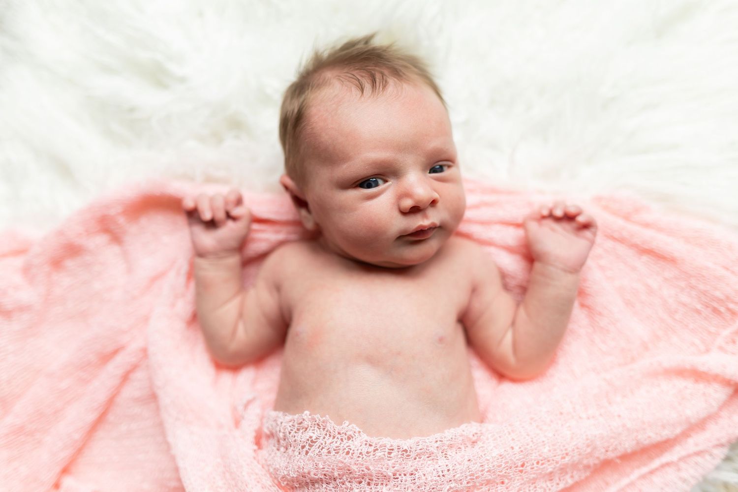 A newborn baby wrapped in a soft pink towel making an adorable expression.