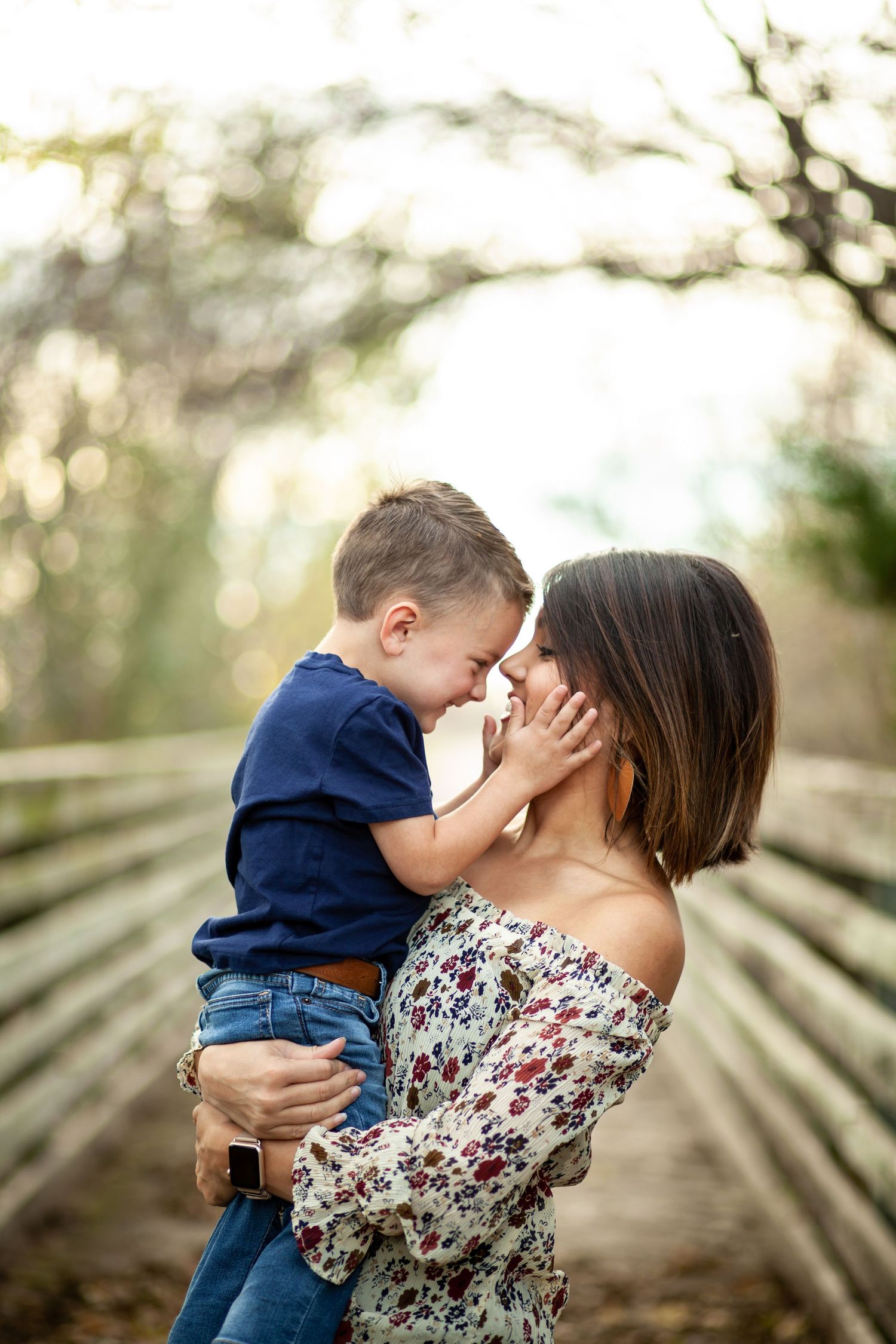 A tender moment between parent and child on a wooden bridge surrounded by nature.