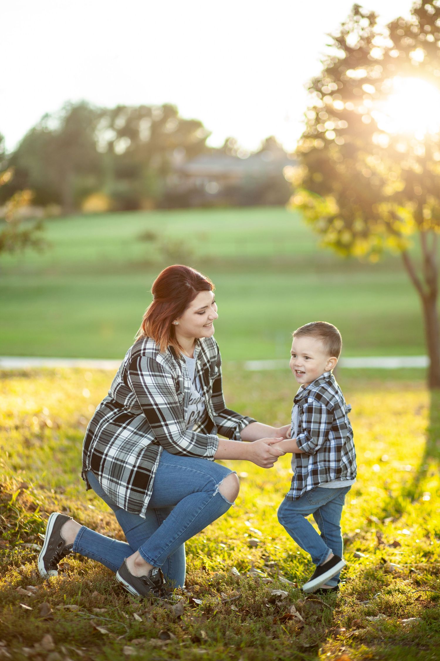 Wearing matching plaid shirts, two figures play together on grassy field at sunset during golden hour.