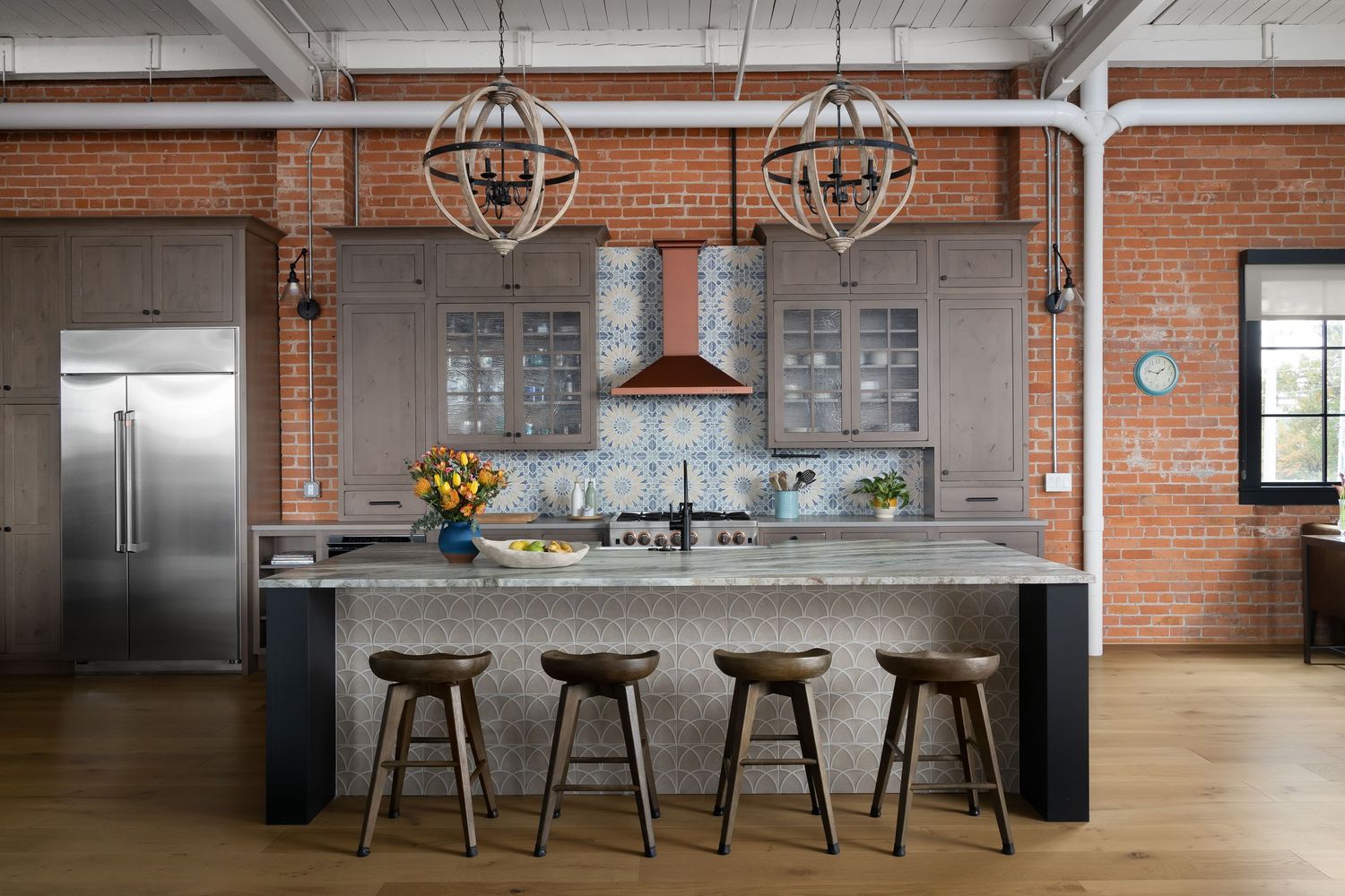 Industrial loft kitchen with exposed brick, pendant lighting, and dark granite island in Detroit, designed by GHK Design.