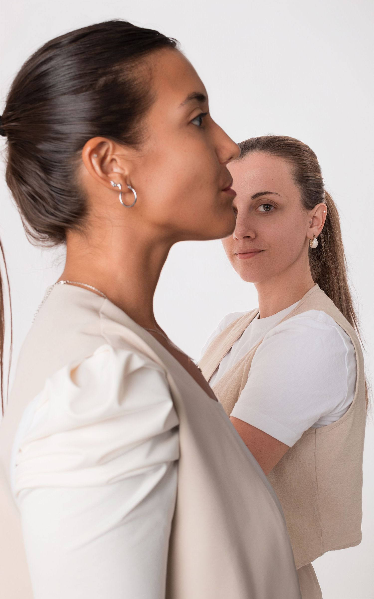 Retrato profesional de dos mujeres con vestimenta neutra posando en estudio sobre fondo blanco.