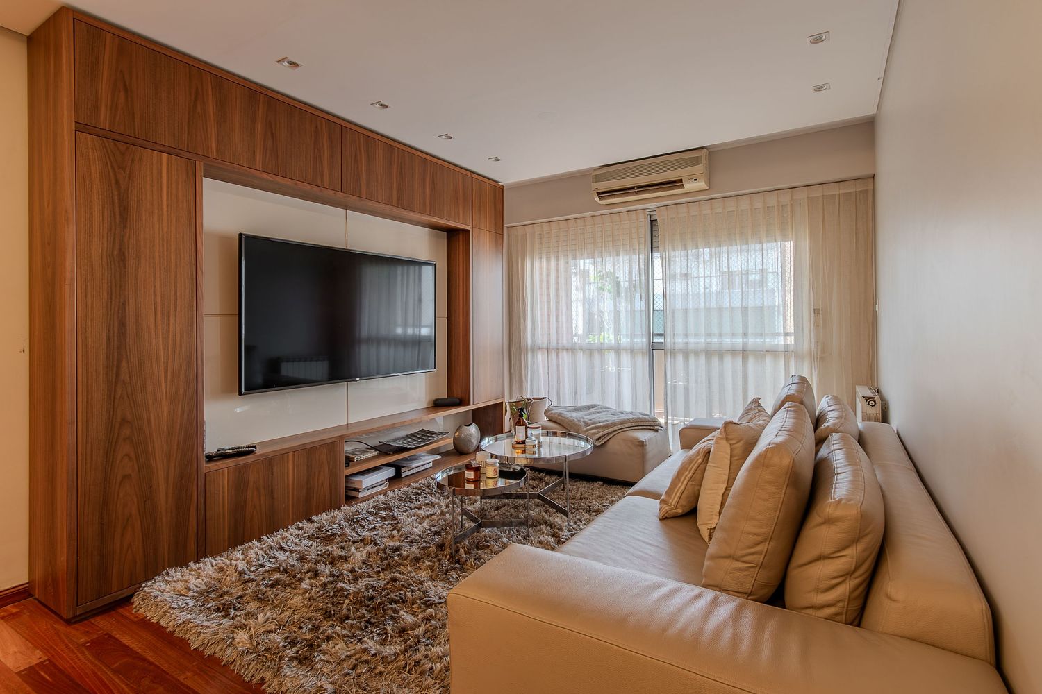 Fotografía inmobiliaria de living moderno con sillón, televisor y luz natural.