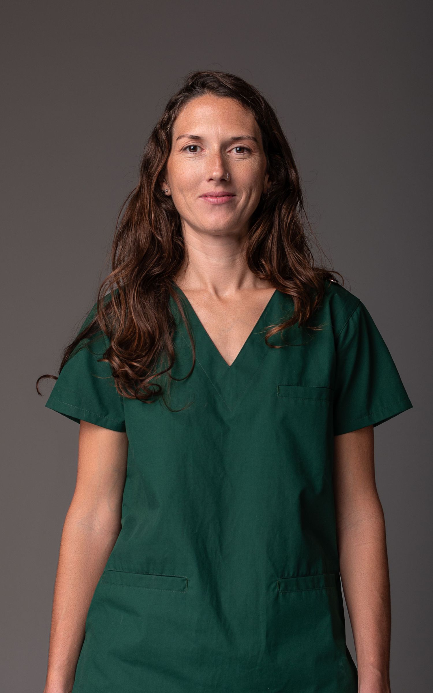Retrato profesional de la salud, mujer con ambo verde posando en estudio sobre fondo gris.
