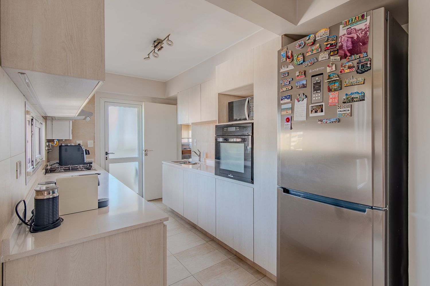 Fotografía de interior para inmobiliaria de cocina amplia con heladera de acero y mobiliario claro.