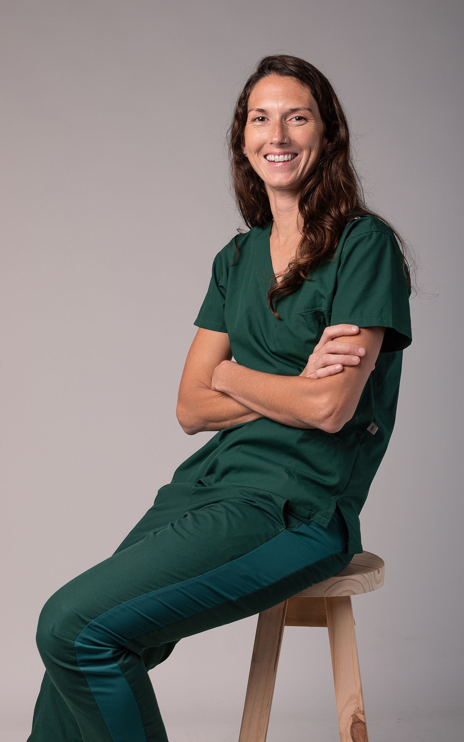 Retrato profesional de mujer médica sentada en banqueta con ambo verde, en estudio sobre fondo claro.