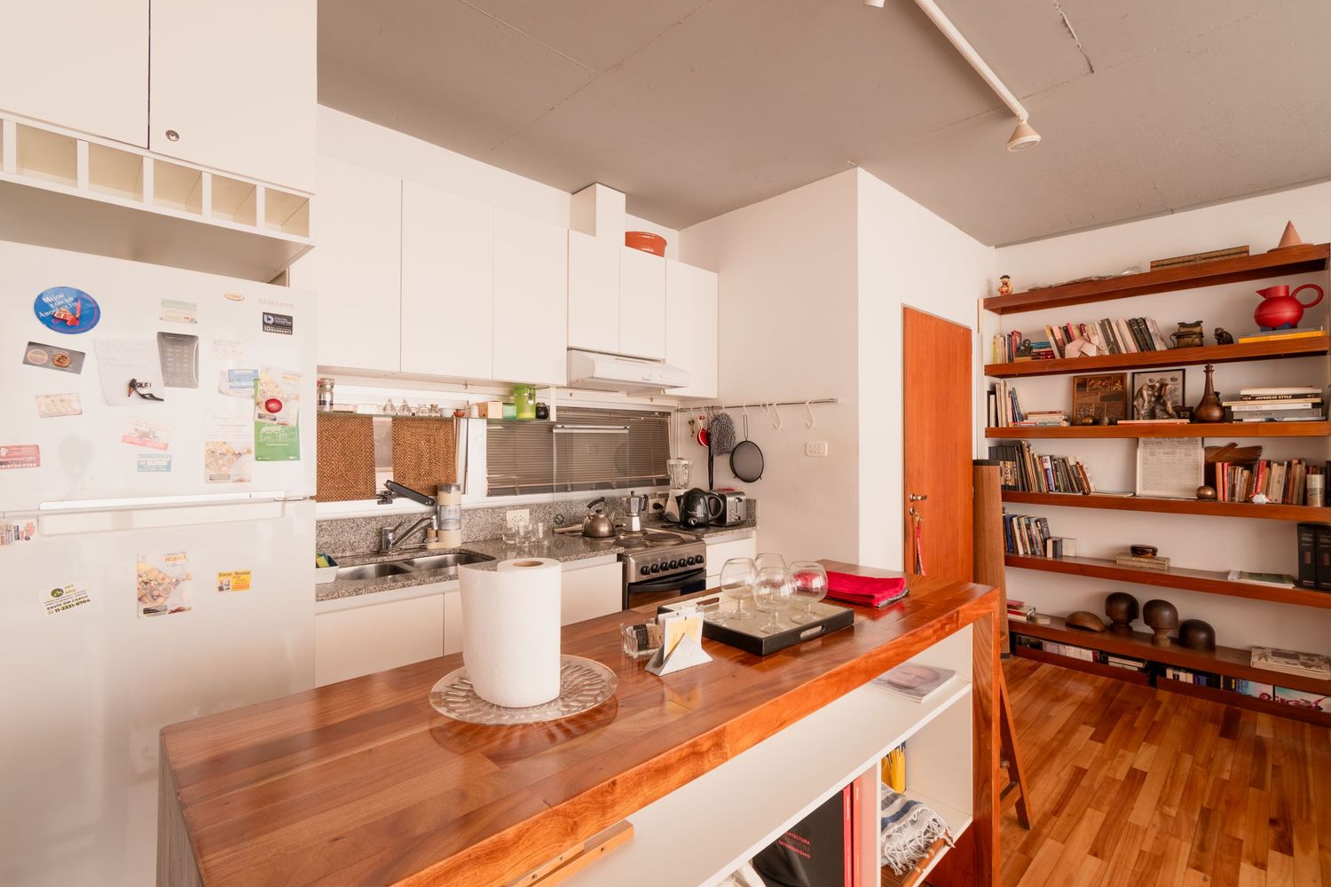 Fotografía profesional para Airbnb de cocina equipada con barra de madera y estanterías abiertas.