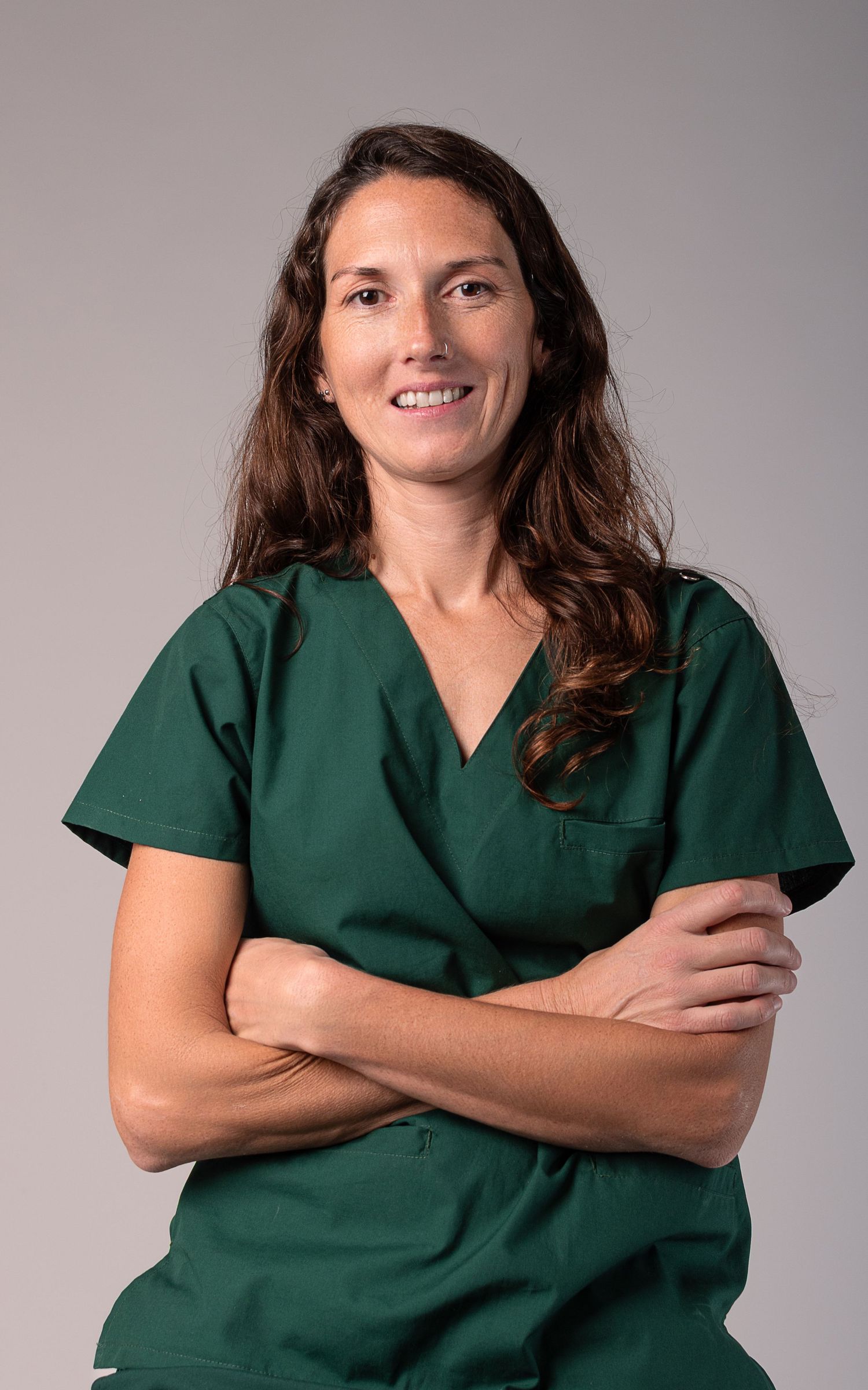 Retrato corporativo de mujer con uniforme médico verde y brazos cruzados sobre fondo neutro.