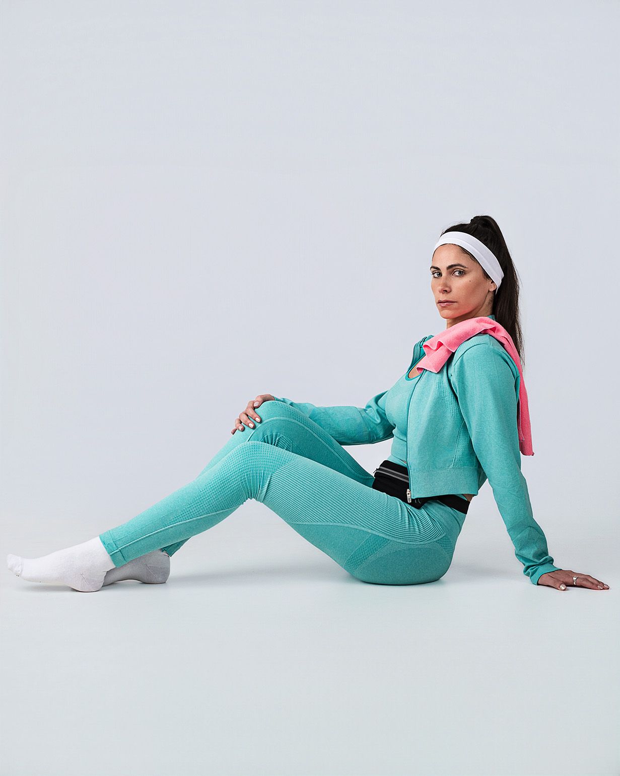 Fotografía e-commerce en estudio de conjunto deportivo turquesa con modelo en pose sentada sobre fondo liso.