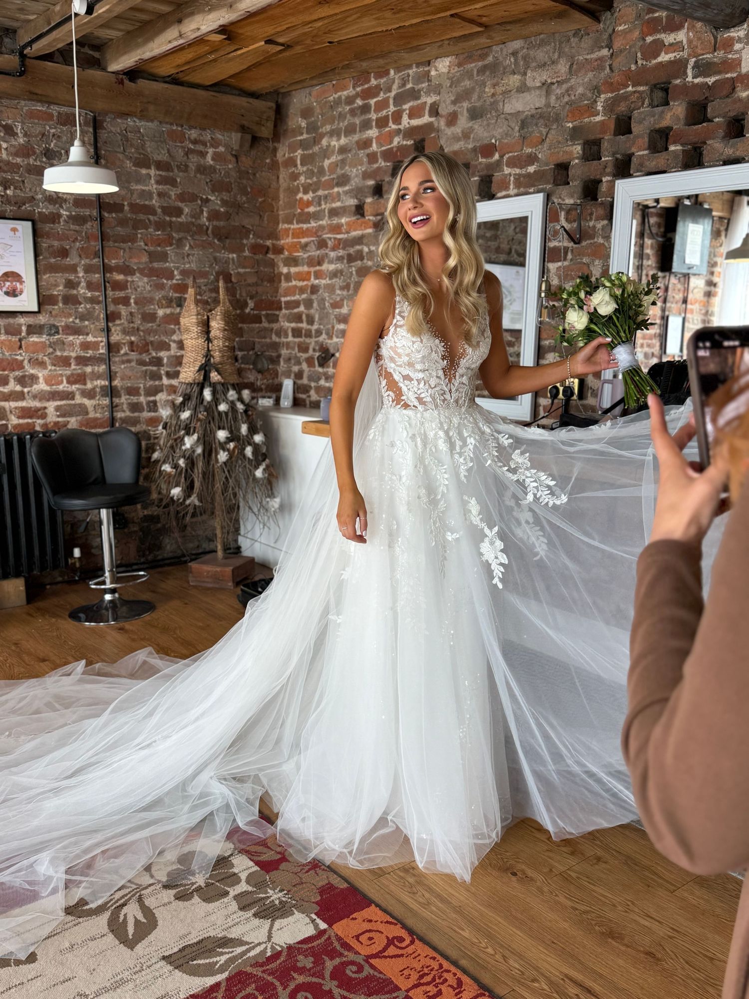 Beautiful white wedding dress with lace details and flowing tulle skirt being photographed in a rustic brick venue.