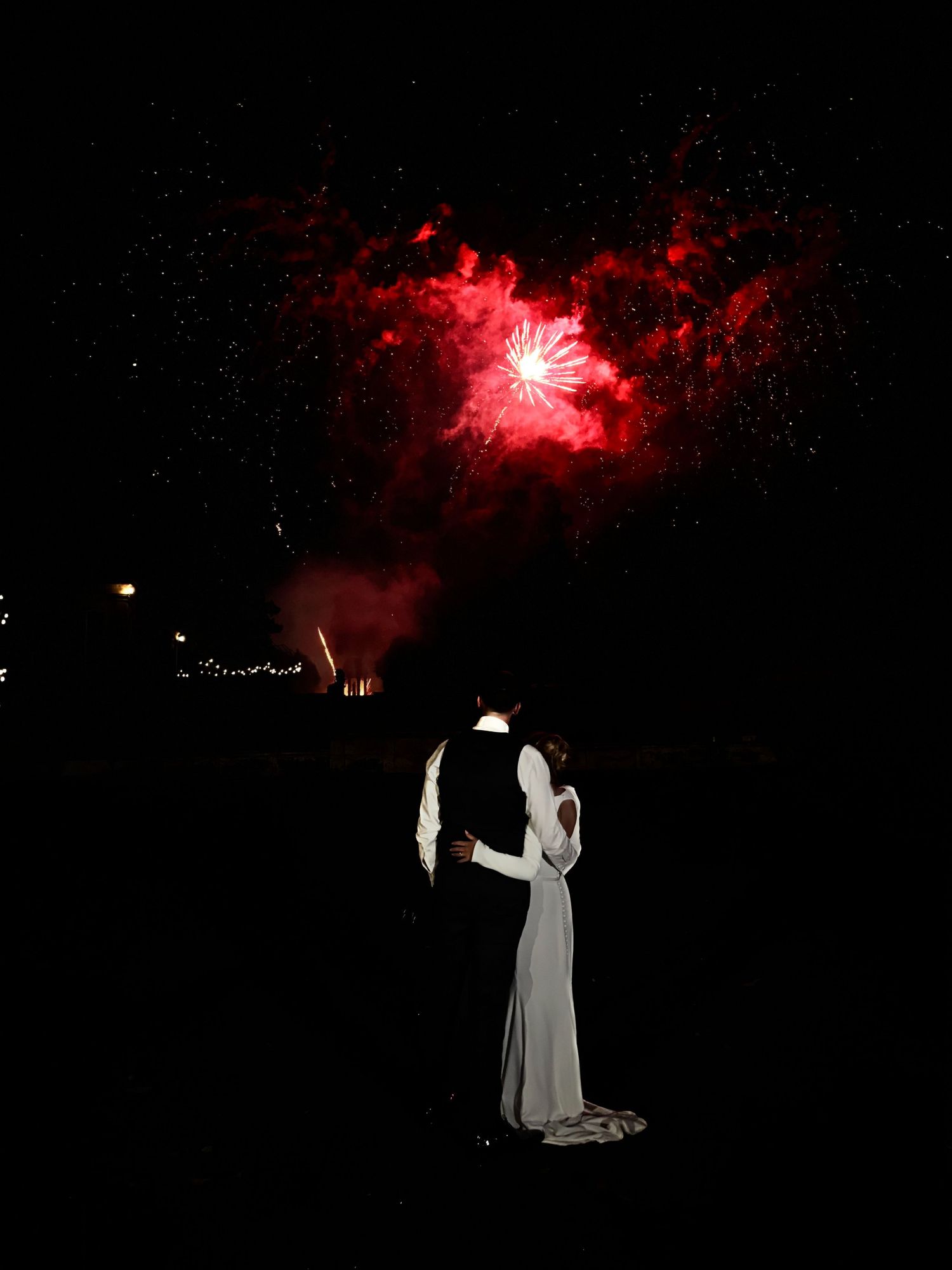 Dramatic silhouettes against red fireworks in the night sky during a romantic moment.