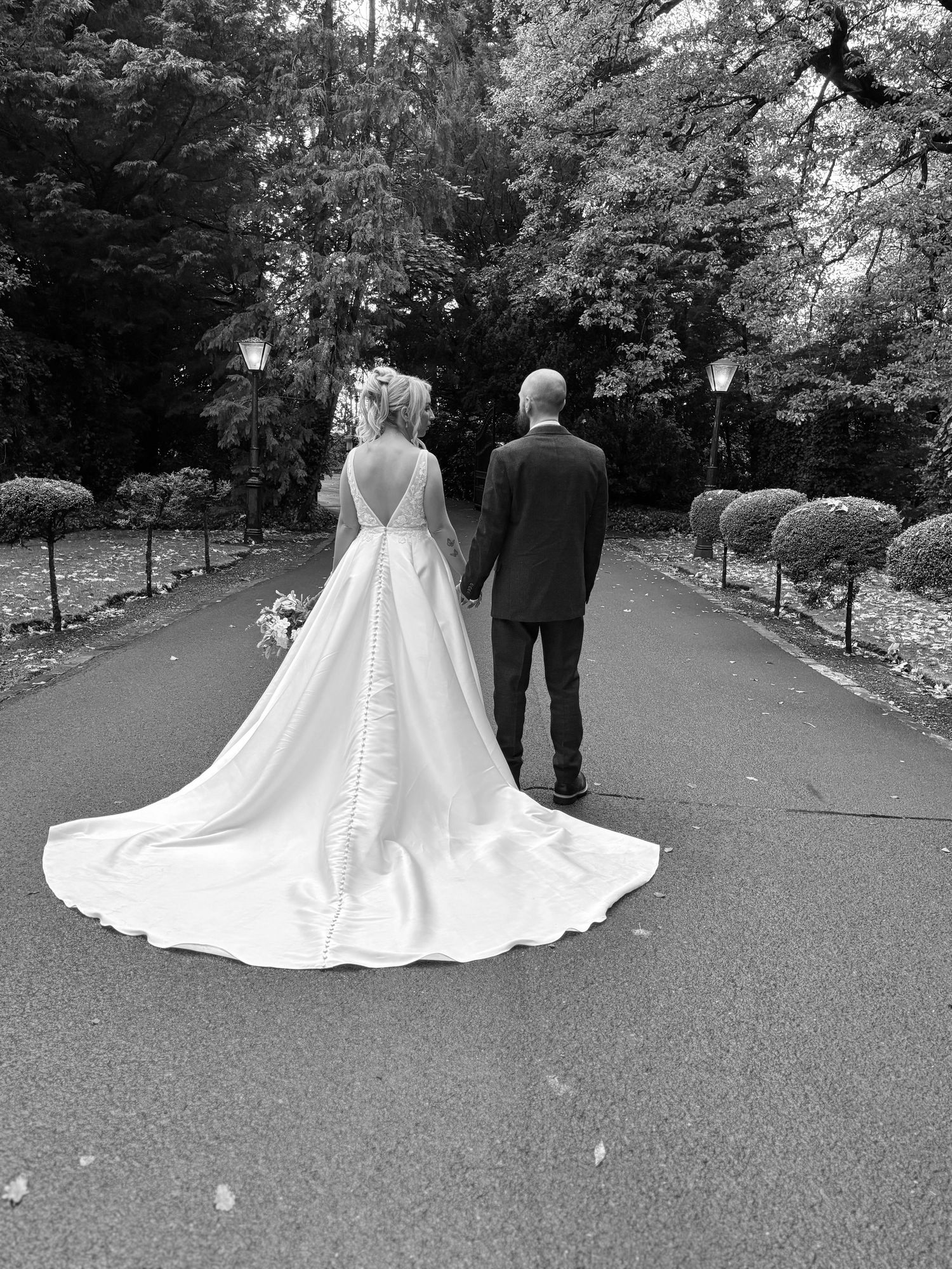 Black and white wedding photos showing a couple walking down a tree-lined path with a flowing white dress train. Wedding cotent