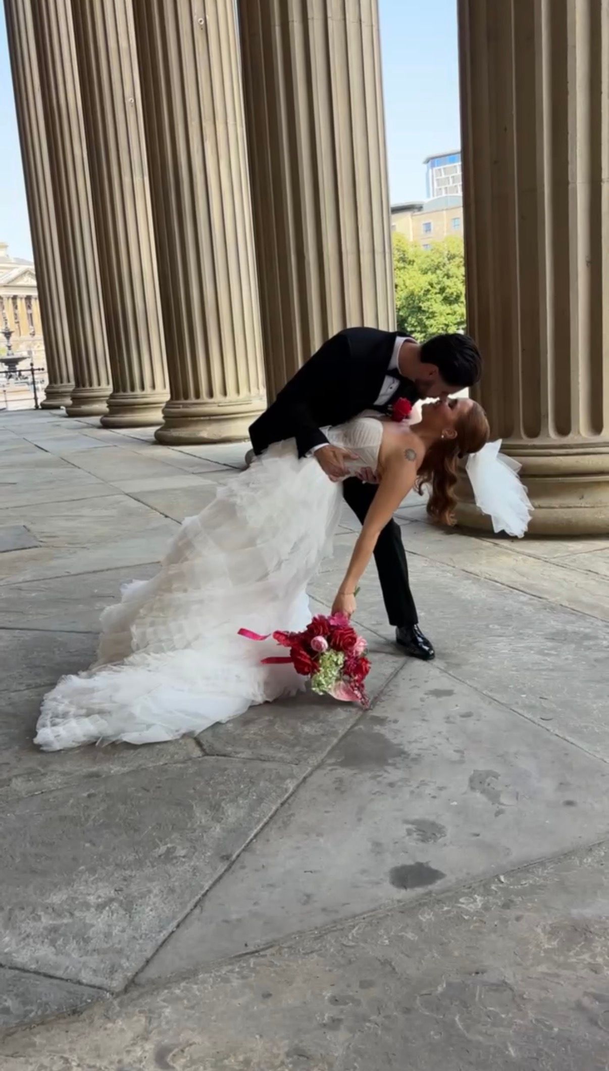 Dramatic dip kiss between newlyweds among classical stone columns.