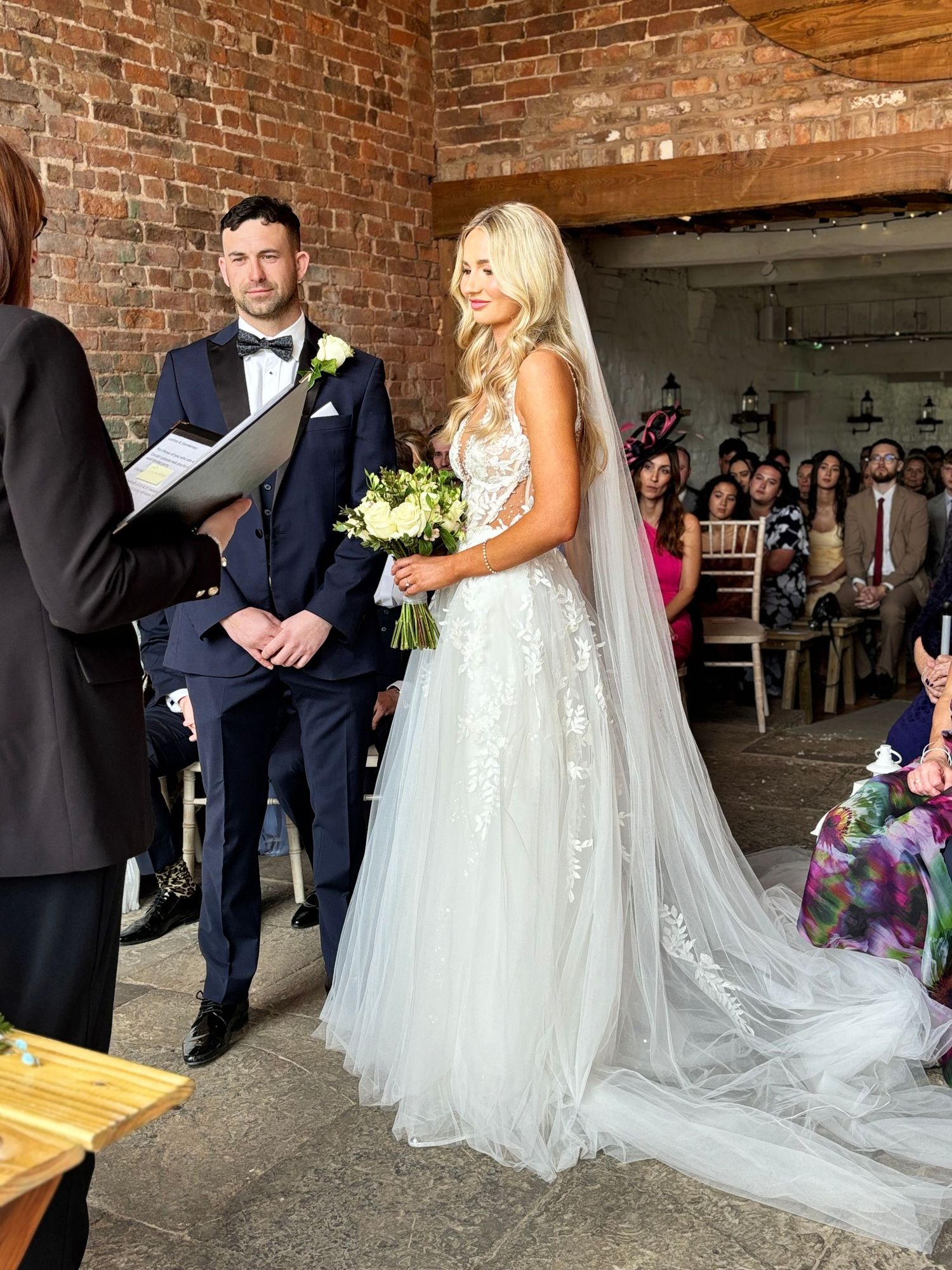 Wedding ceremony in rustic brick venue with guests watching couple exchange vows.