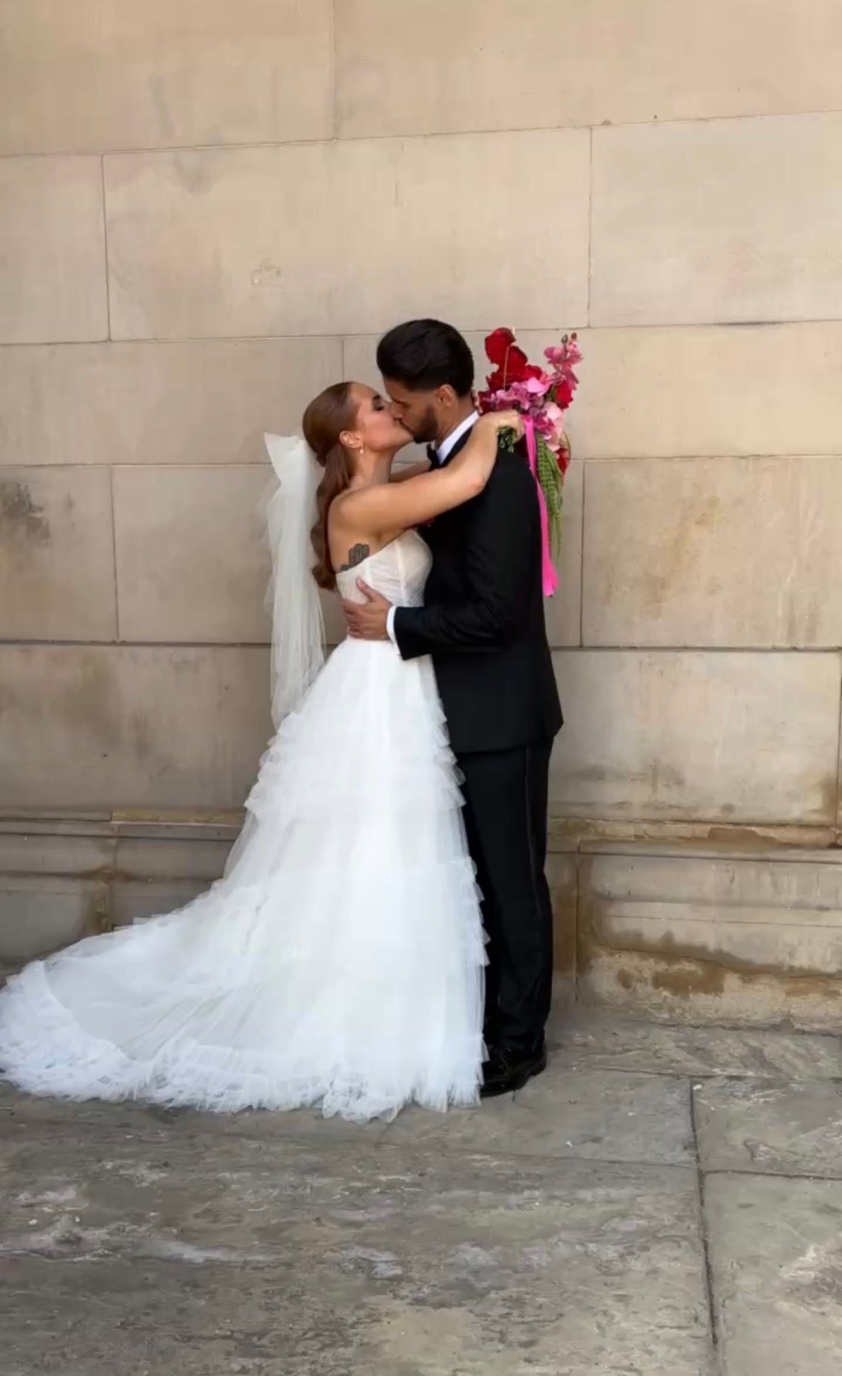 Romantic wedding couple sharing a kiss against stone wall backdrop.