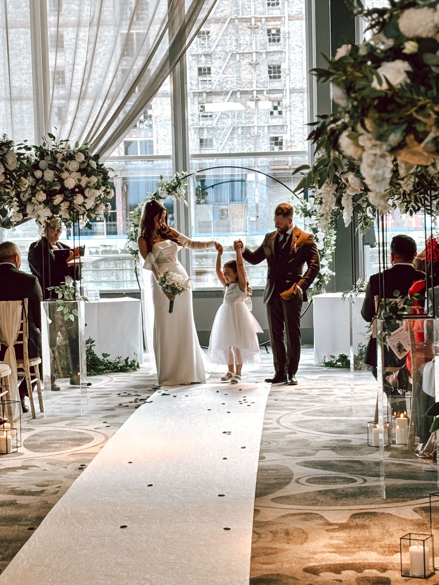 White wedding ceremony setup with floral arrangements and aisle runner in a bright modern venue.