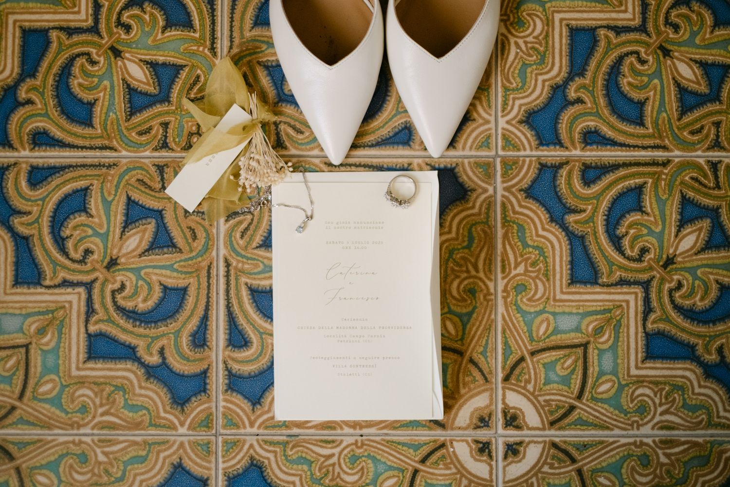 Wedding invitation and white bridal shoes arranged on vintage blue and gold decorative tiles.