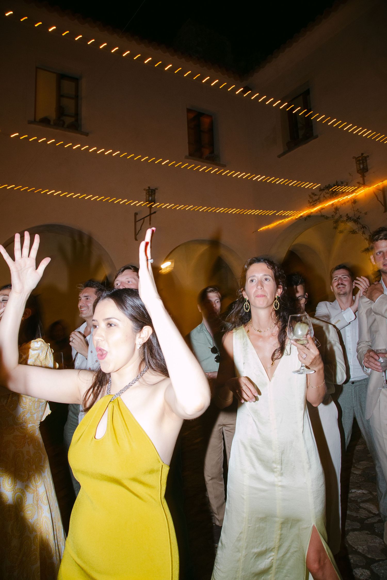Wedding celebration with guests dancing under string lights at night.
